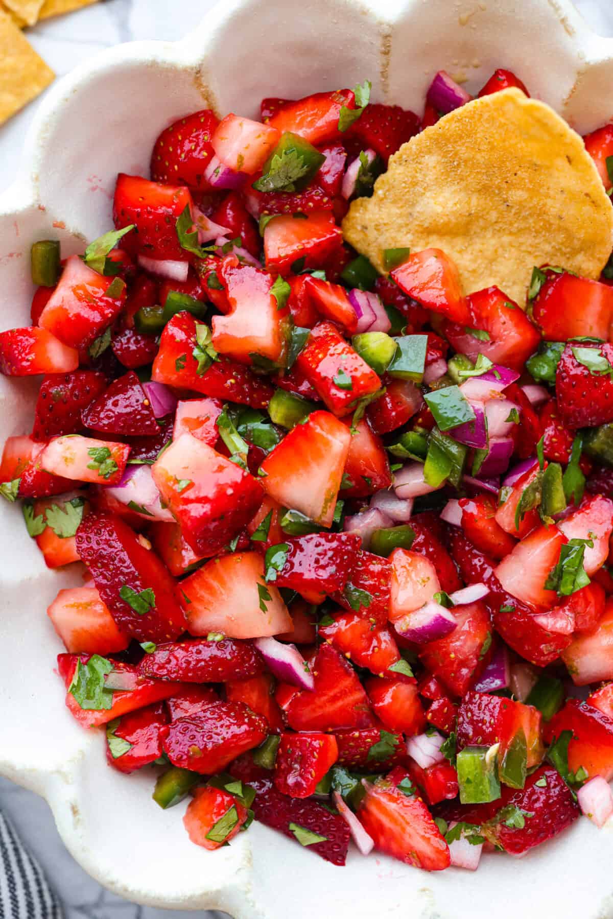 Add a burst of fresh, fruity flavor to your table with this Strawberry Salsa. This quick and easy recipe combines sweet strawberries with a hint of spice and is perfect for a light and refreshing snack in just 10 minutes! A close up of strawberry salsa in a bowl with a chip.