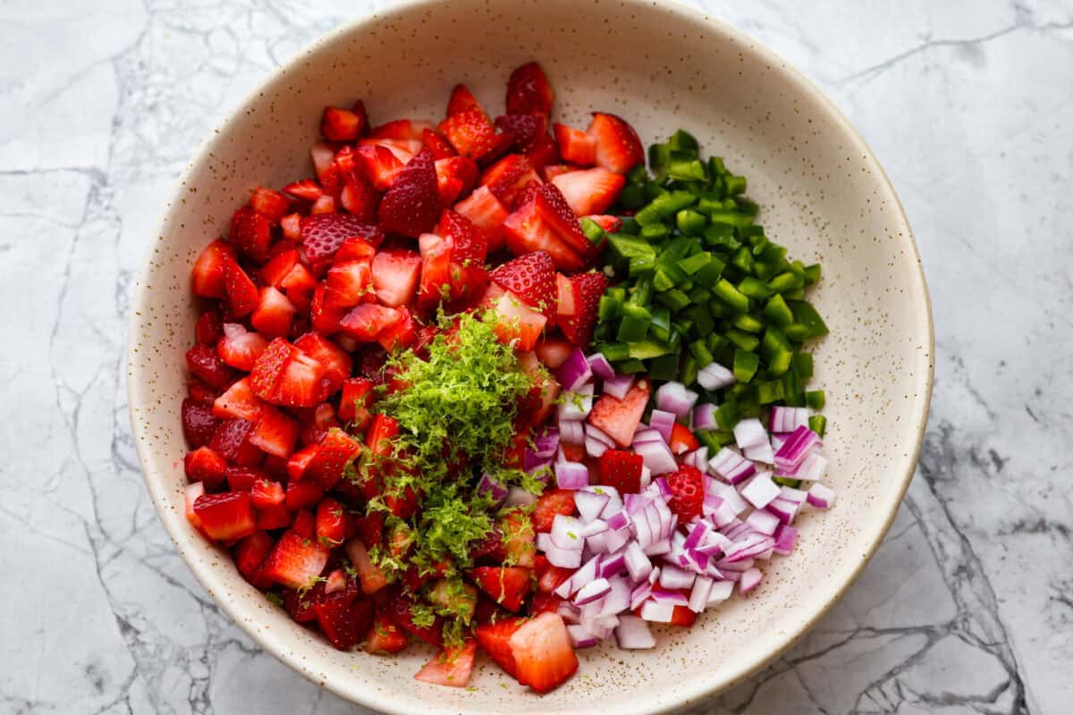 Add a burst of fresh, fruity flavor to your table with this Strawberry Salsa. This quick and easy recipe combines sweet strawberries with a hint of spice and is perfect for a light and refreshing snack in just 10 minutes! Ingredients for strawberry salsa in a bowl.