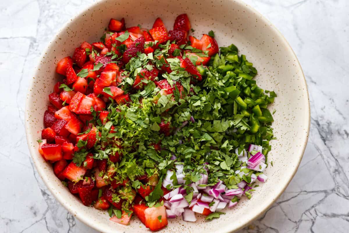 Add a burst of fresh, fruity flavor to your table with this Strawberry Salsa. This quick and easy recipe combines sweet strawberries with a hint of spice and is perfect for a light and refreshing snack in just 10 minutes! Cilantro added to the bowl.