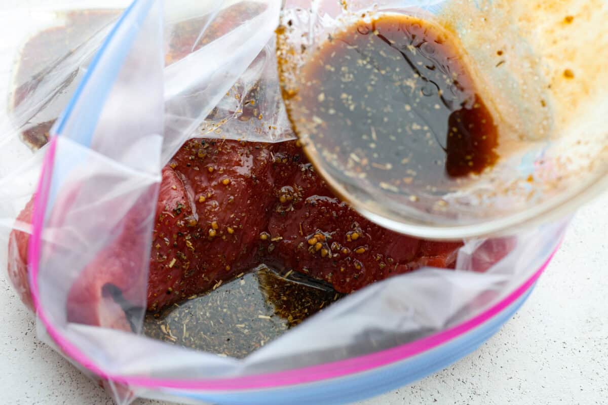 Close up shot of raw tri-tip in large zip-loc with marinade being poured over it. Close up shot of raw tri-tip in large zip-loc with marinade being poured over it.