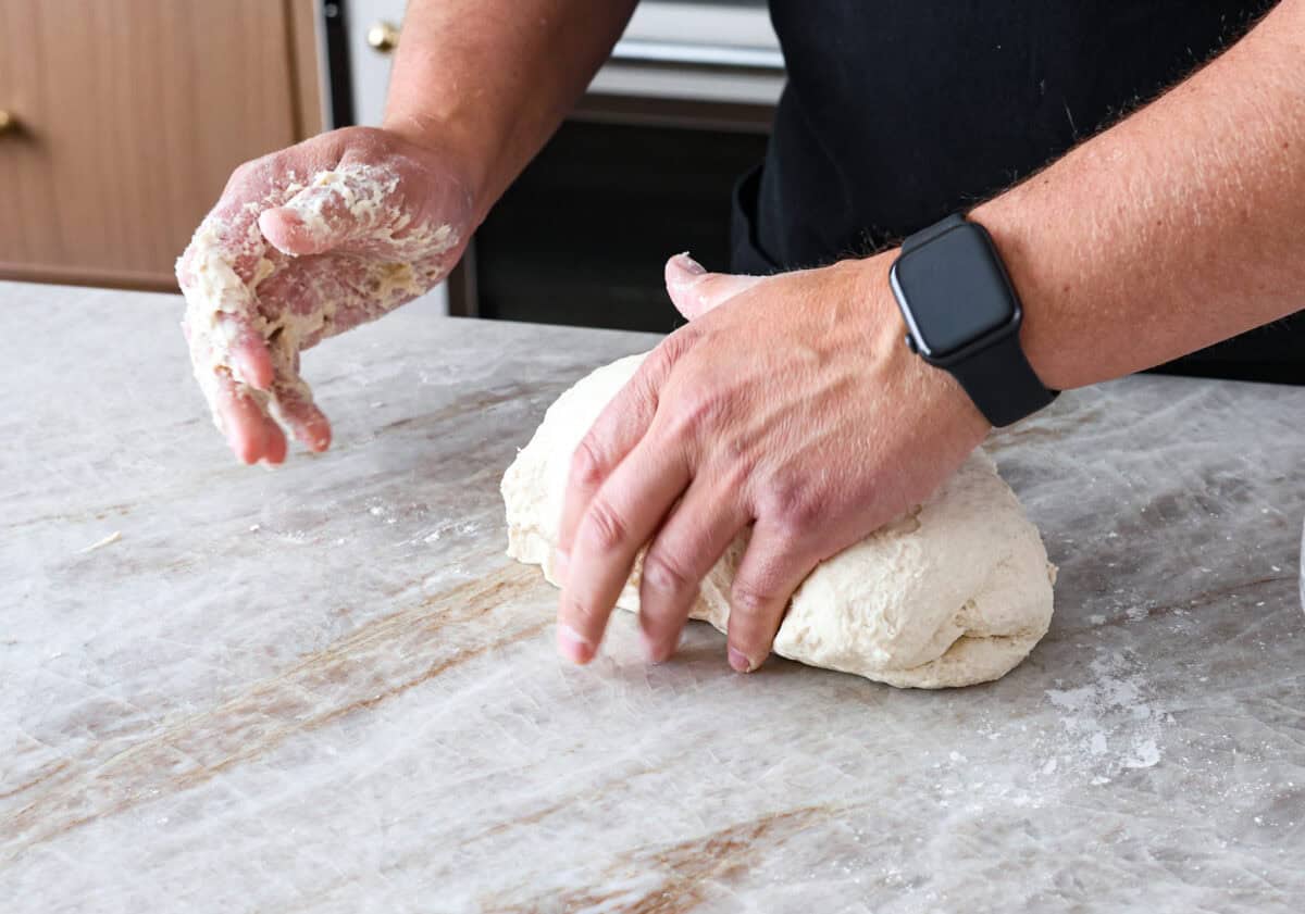 This is the perfect beginner's guide for making wood-fired pizza dough! Pizza expert, Chef Brandon Price, taught me how to make authentic homemade pizza, and now you get to learn too! Fifth photo of shaping and kneading the dough by hand.