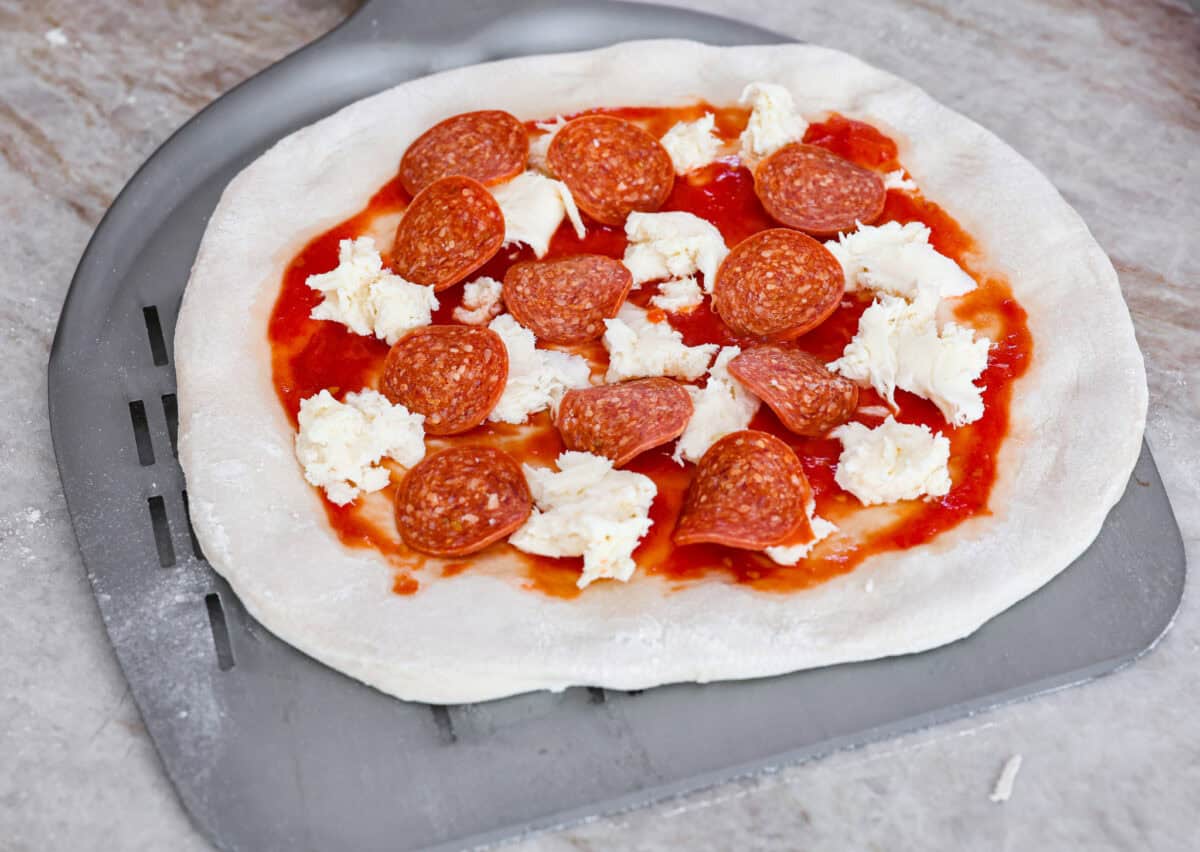 This is the perfect beginner's guide for making wood-fired pizza dough! Pizza expert, Chef Brandon Price, taught me how to make authentic homemade pizza, and now you get to learn too! Fourth photo of the topping added to the pizza and placed on a pizza spatula.