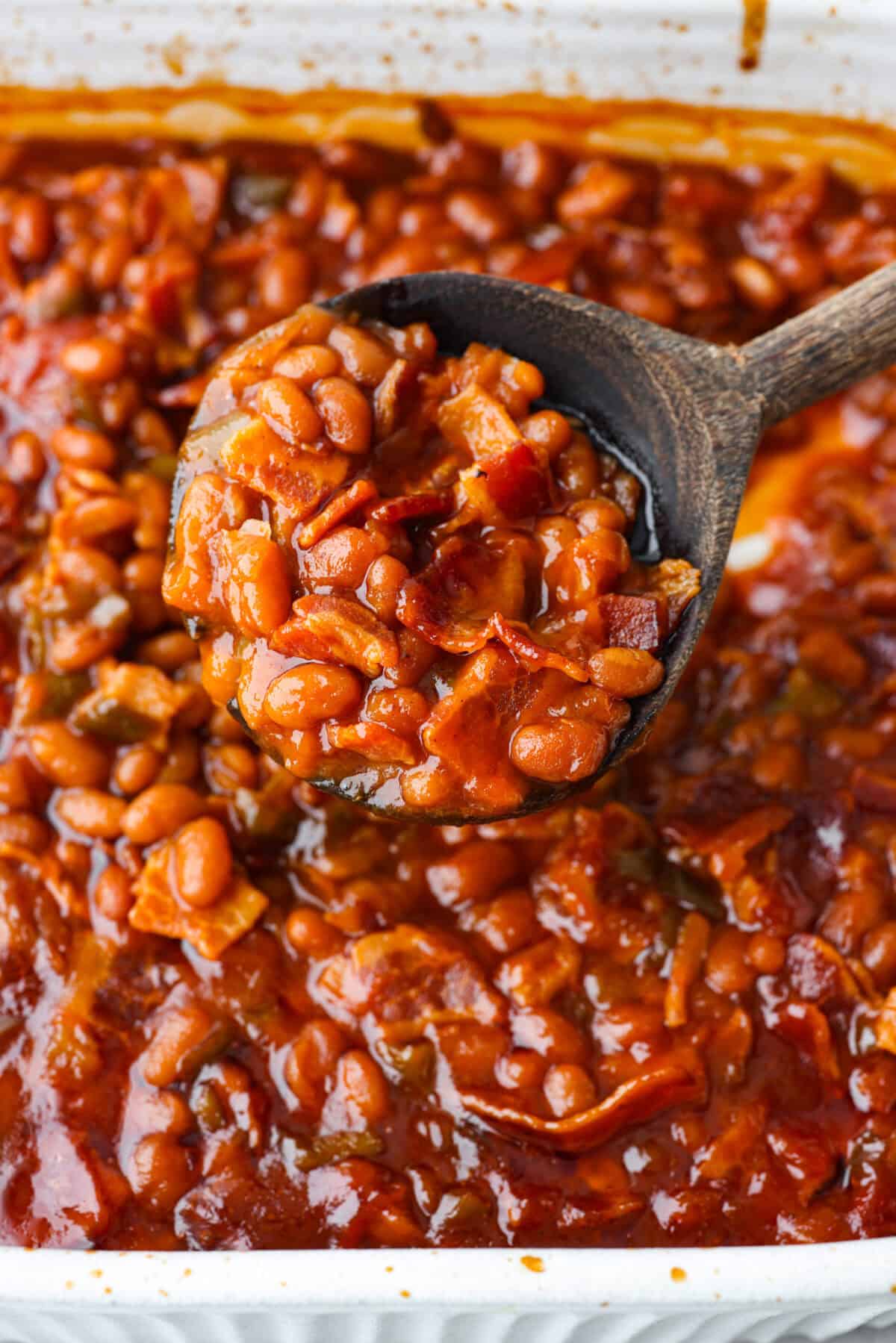 These World's Best Baked Beans will be the last recipe you will ever make! This easy recipe is the perfect side to a potluck and a tried and true family recipe that your family will go crazy over! Close view of the baked beans spooned with a wooden spoon.