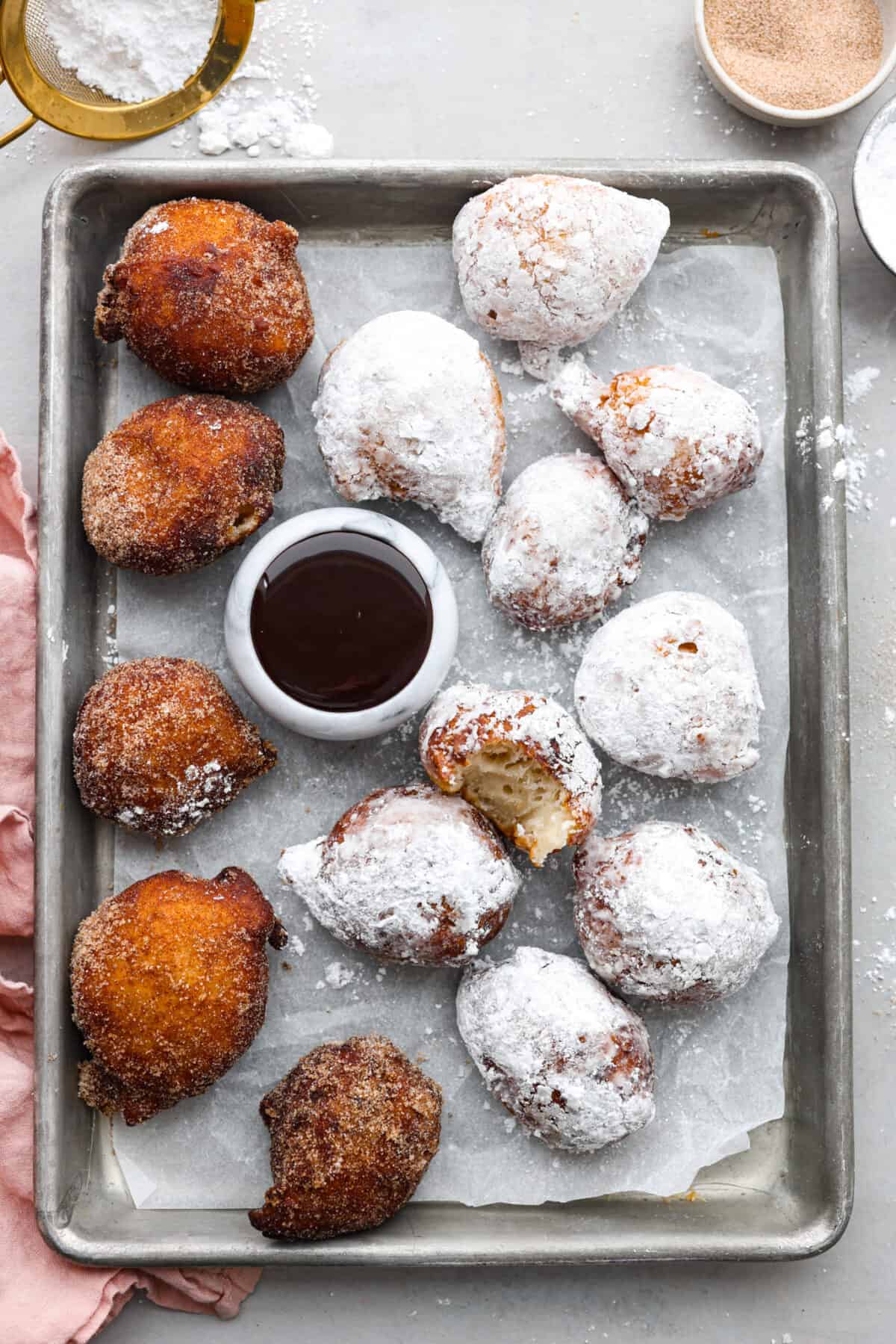 Whip up a batch of these delightful zeppole, perfect for a sweet treat anytime! With a light, fluffy texture and a generous coating of powdered or cinnamon sugar, these Italian donuts are sure to please. Overhead shot of a pan of italian donuts. Some are coated in powdered sugar and others in cinnamon and sugar.