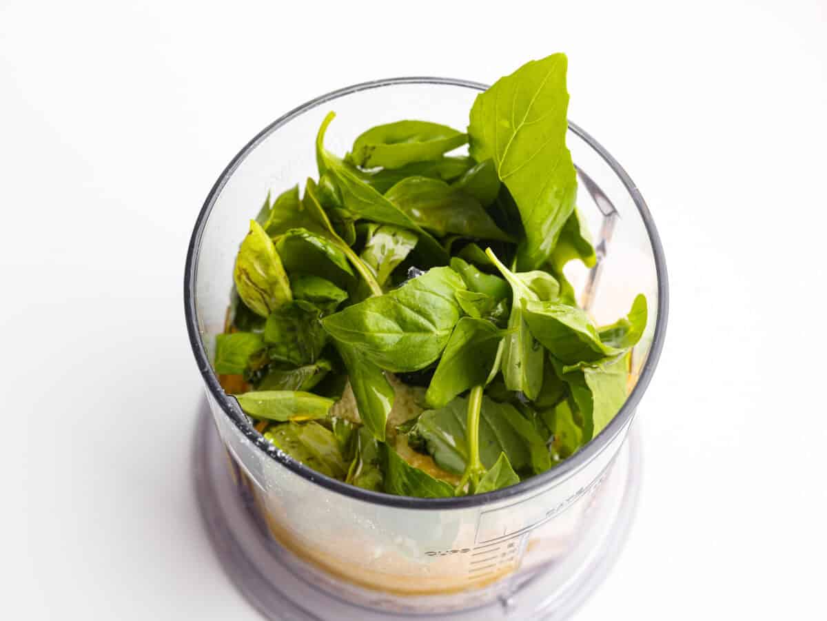 Basil Vinaigrette is a versatile dressing made from a few fresh ingredients. It is bursting with flavor and can be used on salads, as a marinade, or as a sauce for various dishes. It will be a great addition to your repertoire of homemade dressings. Overhead shot of all of the basil vinaigrette ingredients in a food processor.