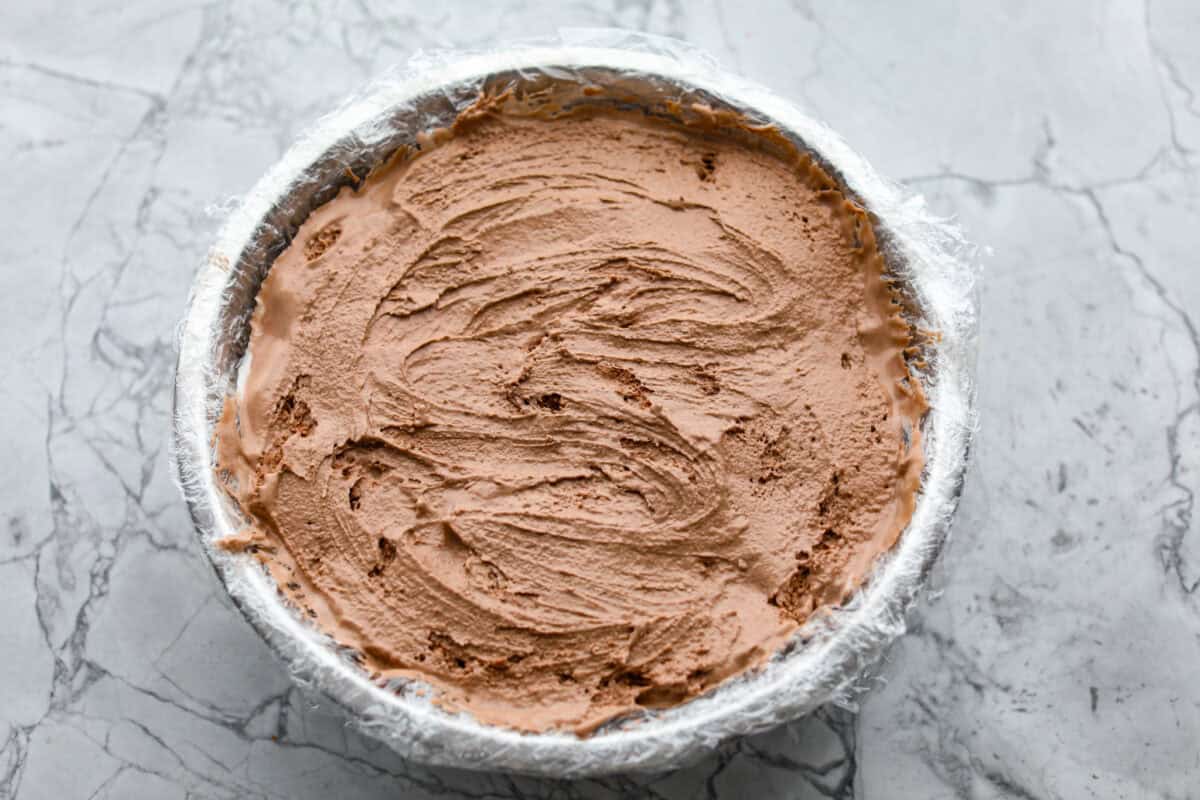 Impress everyone with this gorgeous Baked Alaska dessert! It's surprisingly easy to make with just 5 ingredients. Layers of cake, ice cream and meringue will have your friends and family begging for a slice! Overhead shot of smoothed out ice cream layers in plastic wrapped bowl.