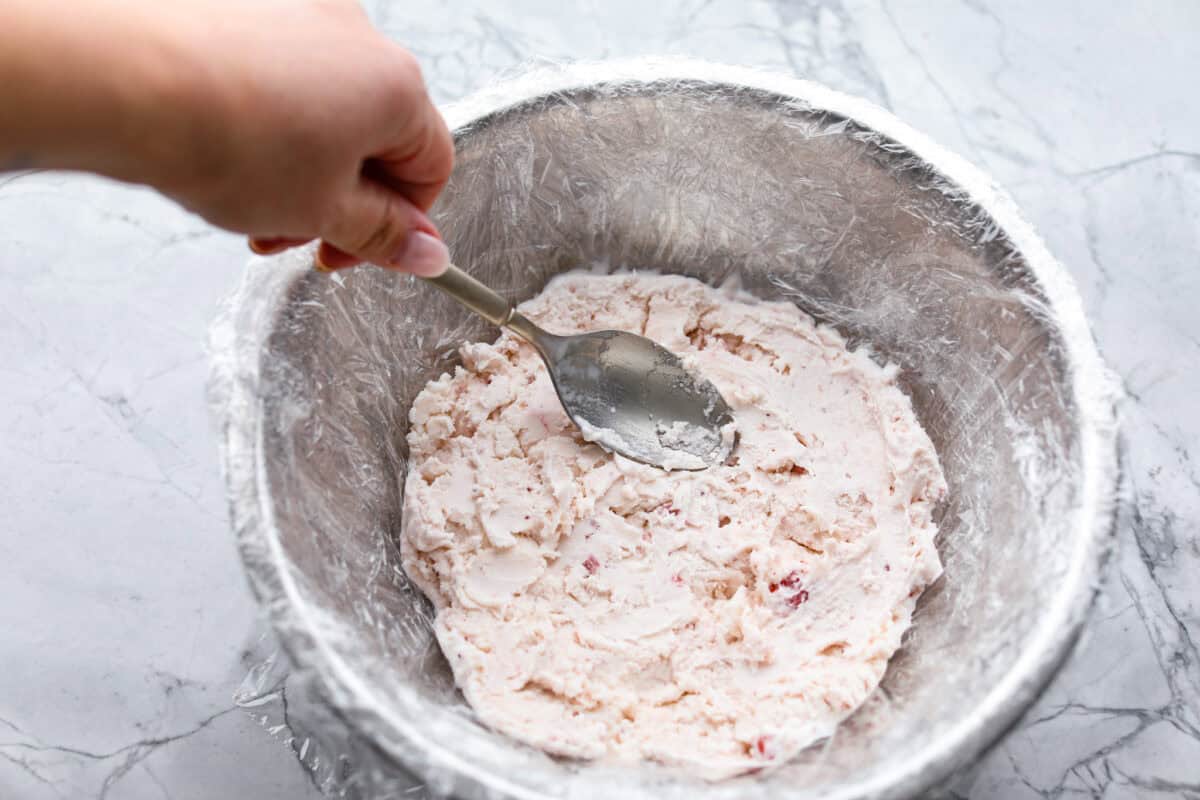 Impress everyone with this gorgeous Baked Alaska dessert! It's surprisingly easy to make with just 5 ingredients. Layers of cake, ice cream and meringue will have your friends and family begging for a slice! Overhead shot of ice cream being spread into the bottom of a plastic wrapped bowl.