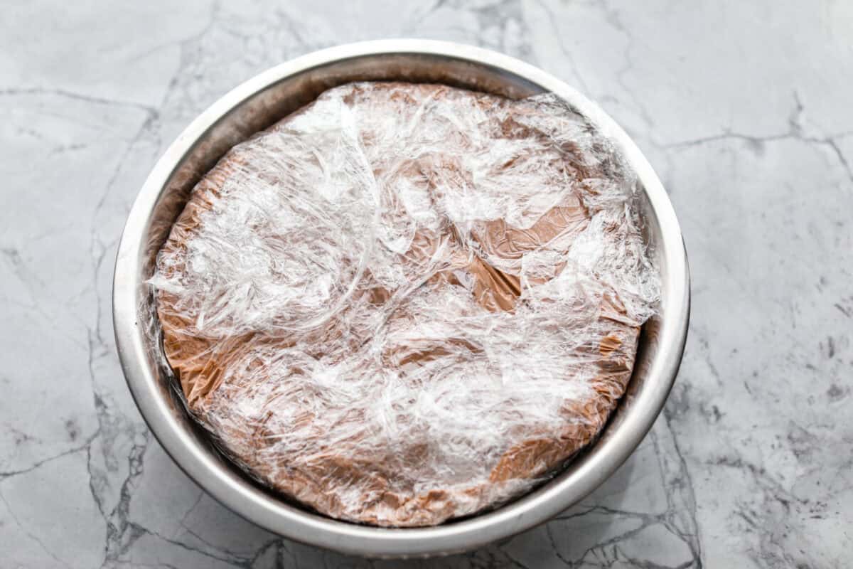 Impress everyone with this gorgeous Baked Alaska dessert! It's surprisingly easy to make with just 5 ingredients. Layers of cake, ice cream and meringue will have your friends and family begging for a slice! Overhead shot of large bowl with ice cream layers and plastic wrap covering the top.