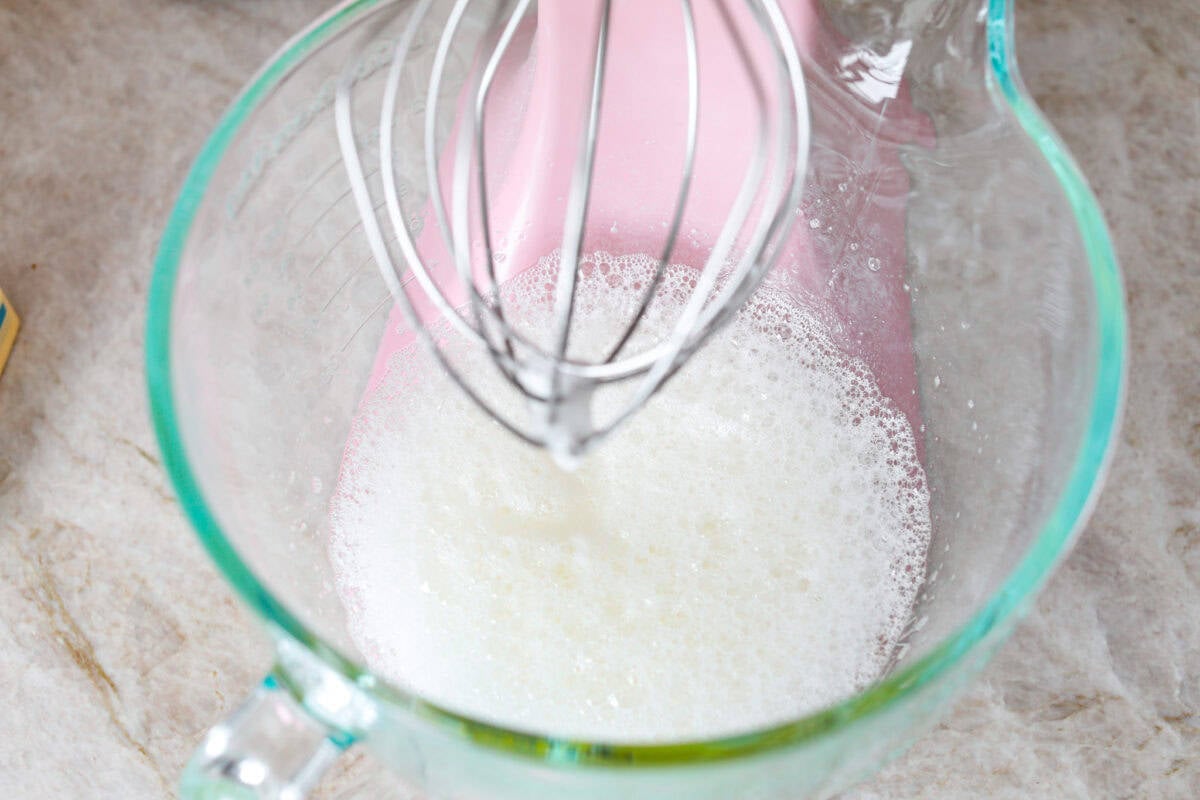 Impress everyone with this gorgeous Baked Alaska dessert! It's surprisingly easy to make with just 5 ingredients. Layers of cake, ice cream and meringue will have your friends and family begging for a slice! Overhead shot of stand mixer with foamy egg whites in bowl.