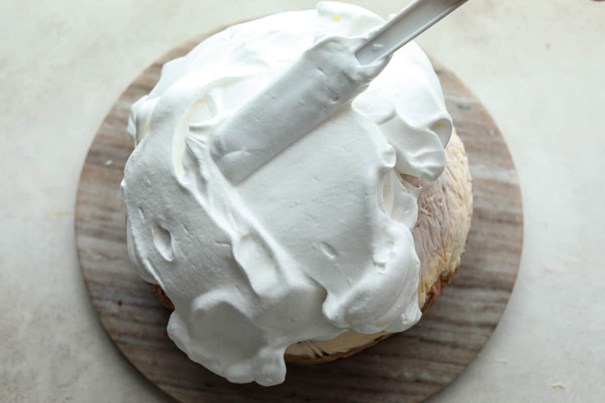 Impress everyone with this gorgeous Baked Alaska dessert! It's surprisingly easy to make with just 5 ingredients. Layers of cake, ice cream and meringue will have your friends and family begging for a slice! Overhead shot of meringue being spread over ice cream and cake of baked Alaska.
