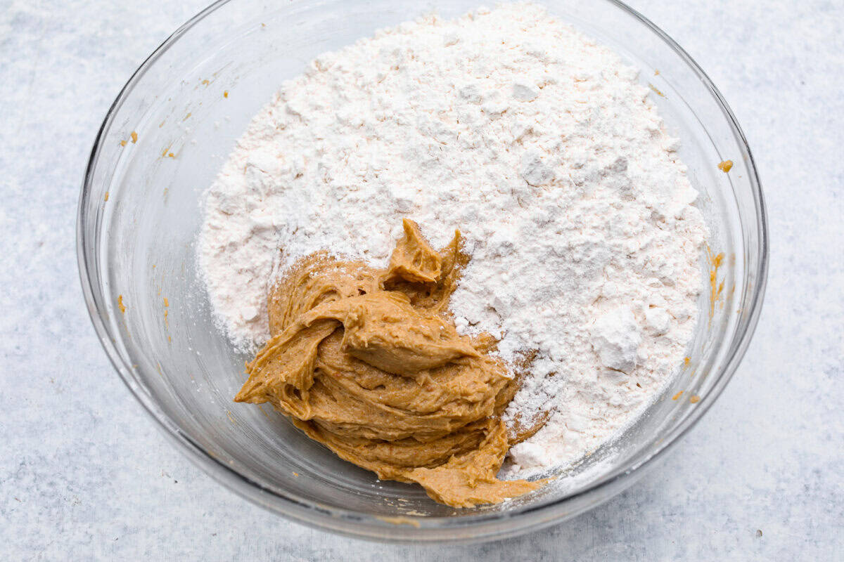 Satisfy your sweet tooth with loaded Biscoff Cookies. They are soft and chewy and infused with the flavor of Biscoff cookies and cookie butter. These are easy to whip up and will be a hit for any occasion! Overhead shot of bowl of cookie dough with dry ingredients on top.
