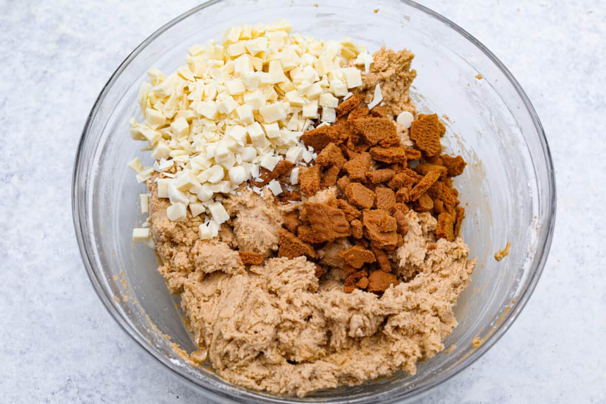 Satisfy your sweet tooth with loaded Biscoff Cookies. They are soft and chewy and infused with the flavor of Biscoff cookies and cookie butter. These are easy to whip up and will be a hit for any occasion! Overhead shot of bowl with Biscoff cookie bits, chunks of white chocolate over cookie dough.