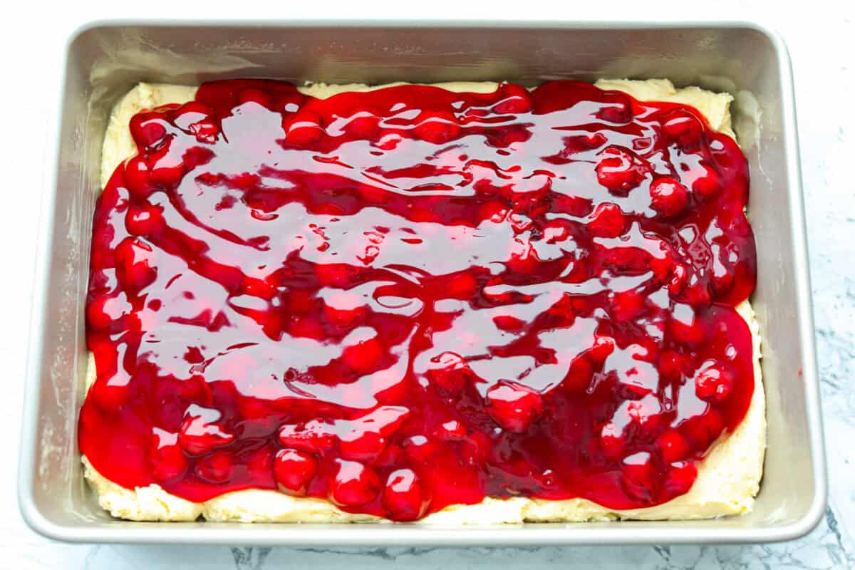 Enjoy cherry pie in its best form: cherry pie bars! You can whip up a whole pan in minutes using cherry pie filling. They’re beautiful, easy to make, and always a crowd-pleaser! Cherry pie filling added to the top of the batter.