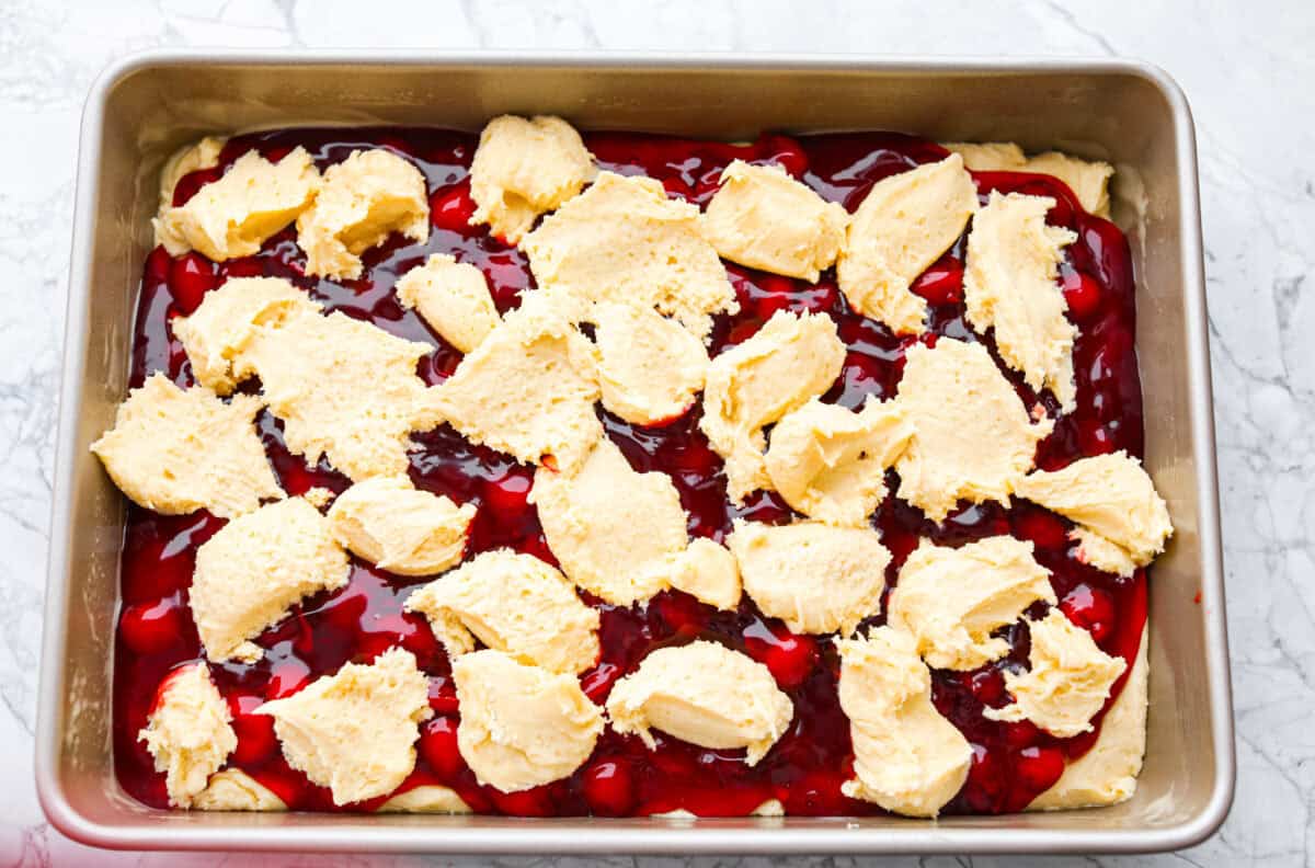 Enjoy cherry pie in its best form: cherry pie bars! You can whip up a whole pan in minutes using cherry pie filling. They’re beautiful, easy to make, and always a crowd-pleaser! Remaining batter being spooned on top of the pie filling just before baking the cherry pie bars.