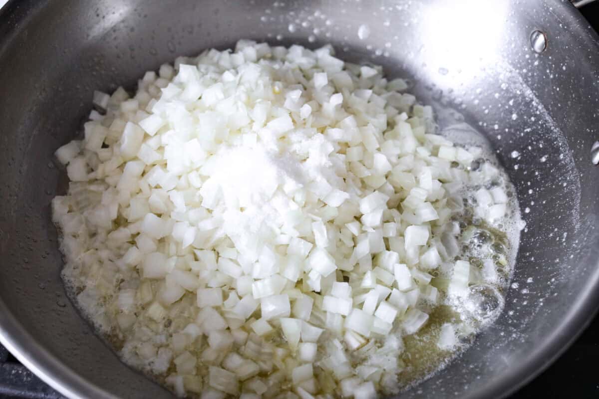 The Best French Onion Dip begins with caramelized onions that combine with cream cheese, sour cream, and seasonings. It creates a dip so addictive and creamy, it'll be gone before you know it! First photo of onions, butter, sugar, and salt in a pan.