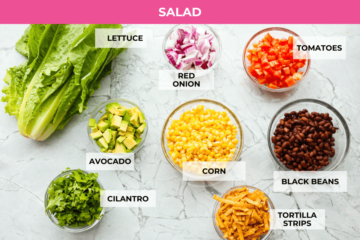 Beef taco salad is a delicious and simple family favorite, perfect for summer evenings! Packed with your favorite taco essentials like beans, corn, avocado, and fresh cilantro, it's bursting with flavor and sure to become a staple dish! Overhead shot of labeled salad ingredients.