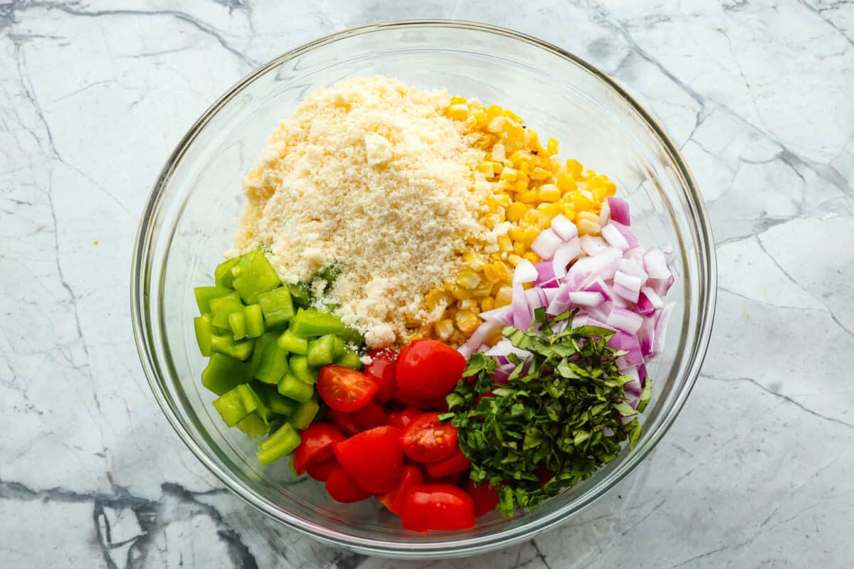This Italian Corn Salad is bursting with fresh flavors from sweet corn, juicy grape tomatoes, crisp green bell pepper, and sharp parmesan cheese. Tossed in a zesty homemade Italian dressing, it’s perfect for summer or any time of the year. Overhead shot of glass bowl with salad ingredients divided inside of it.