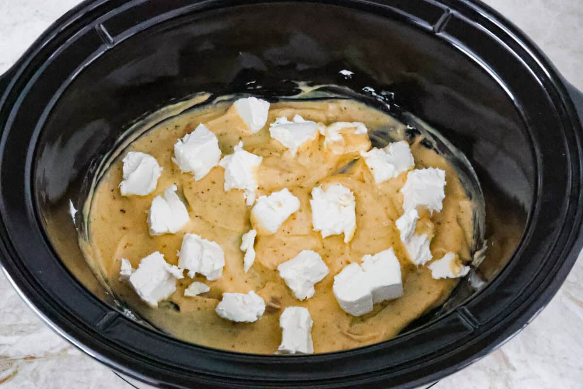 Italian cream cheese chicken is a simple way to enjoy tender, creamy, flavorful chicken over noodles, rice, or potatoes. With only four ingredients, this is definitely one of those slow cooker recipes you will have on repeat. Overhead shot of canned cream of chicken soup mixed with Italian seasoning with cubed cream cheese on top.