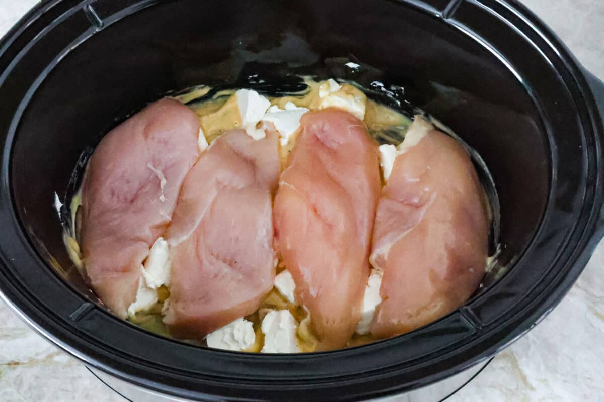 Italian cream cheese chicken is a simple way to enjoy tender, creamy, flavorful chicken over noodles, rice, or potatoes. With only four ingredients, this is definitely one of those slow cooker recipes you will have on repeat. Overhead shot of chicken breasts over cream of chicken and cream cheese.