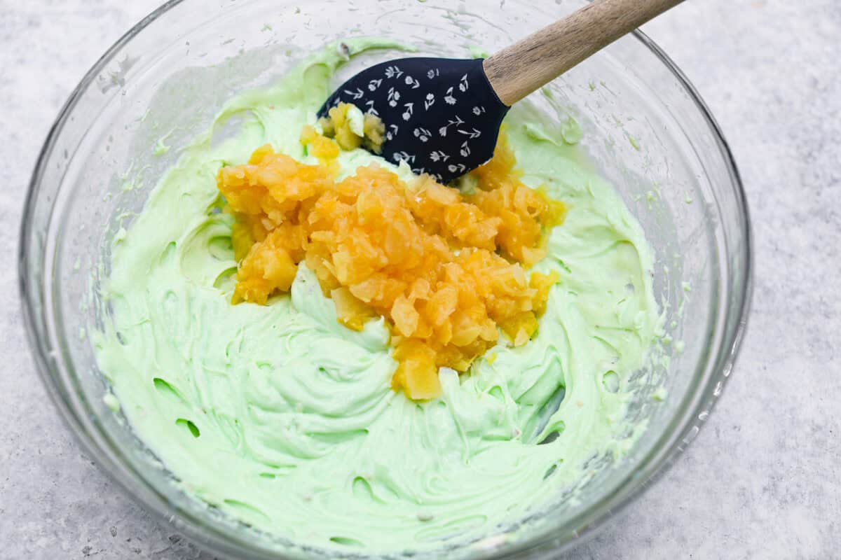 Bring this easy and irresistible no-bake pistachio cream pie to your next gathering! You'll love the combination of the pistachio and pineapple flavors that fill the inside of a sweet, buttery, graham cracker crust. Second photo of the pineapple folding into the creamy filling.