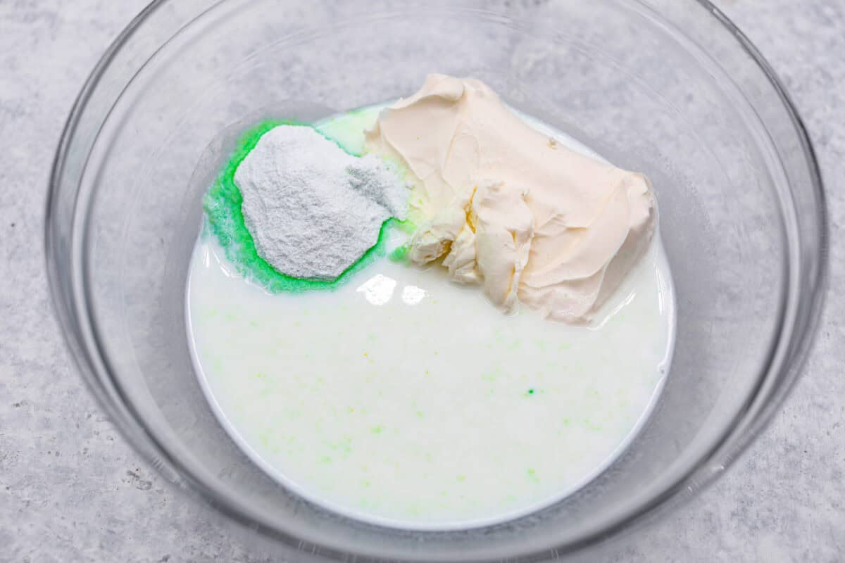 Bring this easy and irresistible no-bake pistachio cream pie to your next gathering! You'll love the combination of the pistachio and pineapple flavors that fill the inside of a sweet, buttery, graham cracker crust. First photo of the milk, cream cheese, and pudding powder in a bowl.