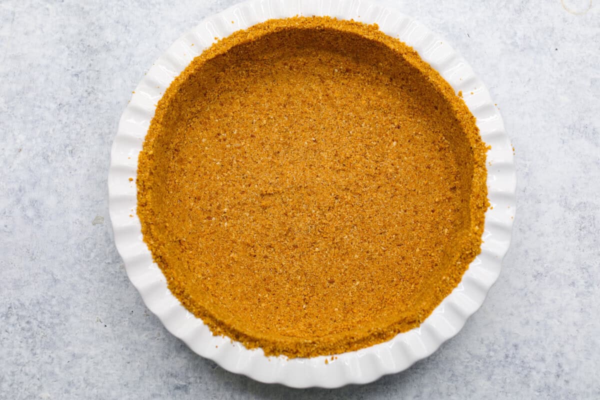 This strawberry cream cheese pie has a smooth, creamy filling is topped with sweet strawberries and is held together by a crumbly, buttery crust. Simply divine! Overhead shot of graham cracker crumb crust in pie dish.