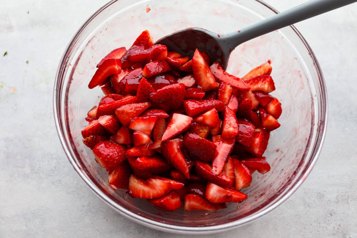 This strawberry cream cheese pie has a smooth, creamy filling is topped with sweet strawberries and is held together by a crumbly, buttery crust. Simply divine! Overhead shot of a large bowl of strawberries being stirred.