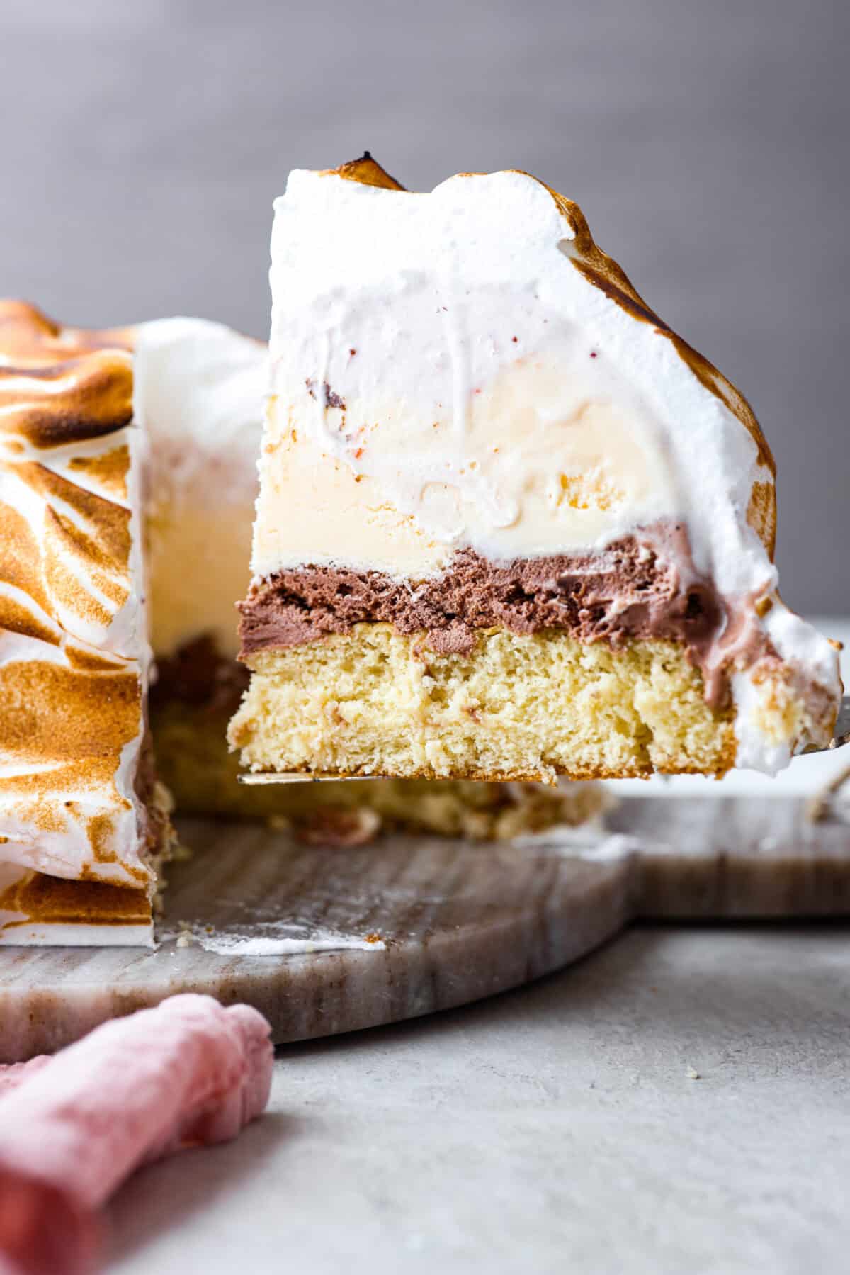 Impress everyone with this gorgeous Baked Alaska dessert! It's surprisingly easy to make with just 5 ingredients. Layers of cake, ice cream and meringue will have your friends and family begging for a slice! Side shot of slice of baked Alaska being served out of the whole cake.