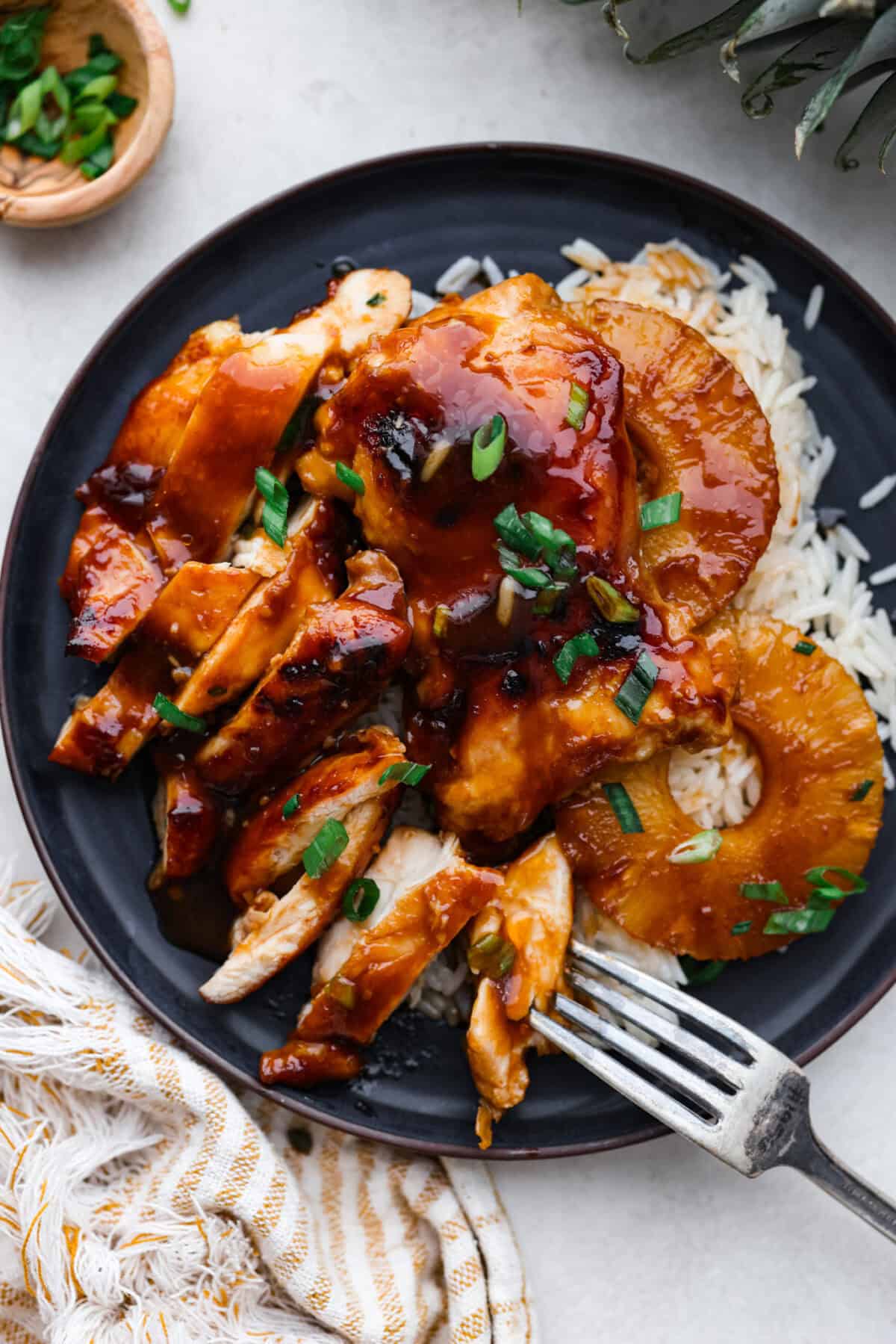 Baked Huli Huli chicken is a tried and true recipe now made in the oven! Tender chicken baked in a sweet and savory sauce. This easy one-pan dinner is full of Hawaiian-inspired flavors! Top view of the chicken sliced and plated with rice.