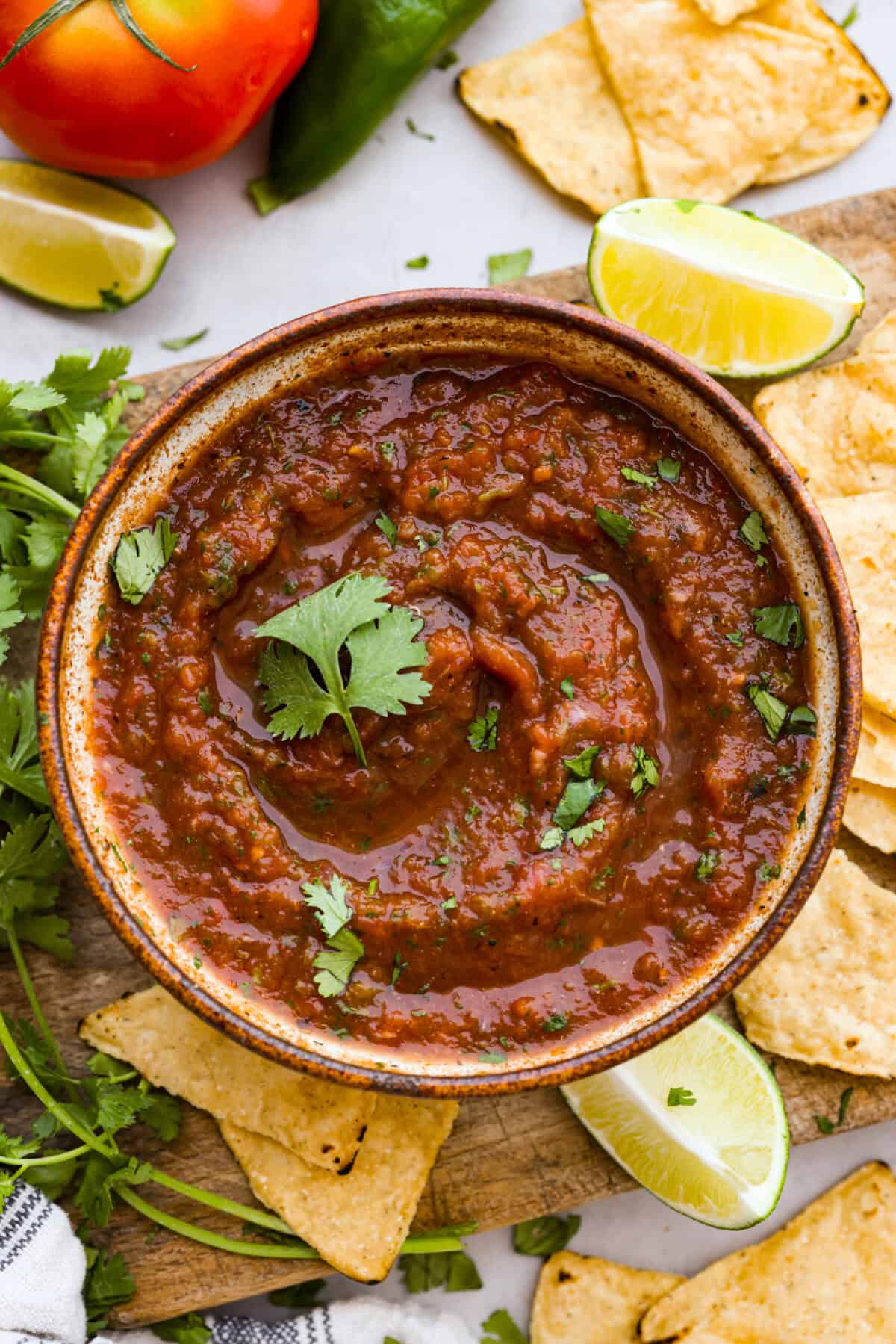 Best Blender Salsa is restaurant-quality salsa that is made right in your blender! It only takes 5 minutes and is truly the very best out there! This vibrant and refreshing salsa has the perfect blend of sweet, spicy elements. Overhead shot of bowl of blender salsa surrounded by limes, tortilla chips and fresh cilantro.
