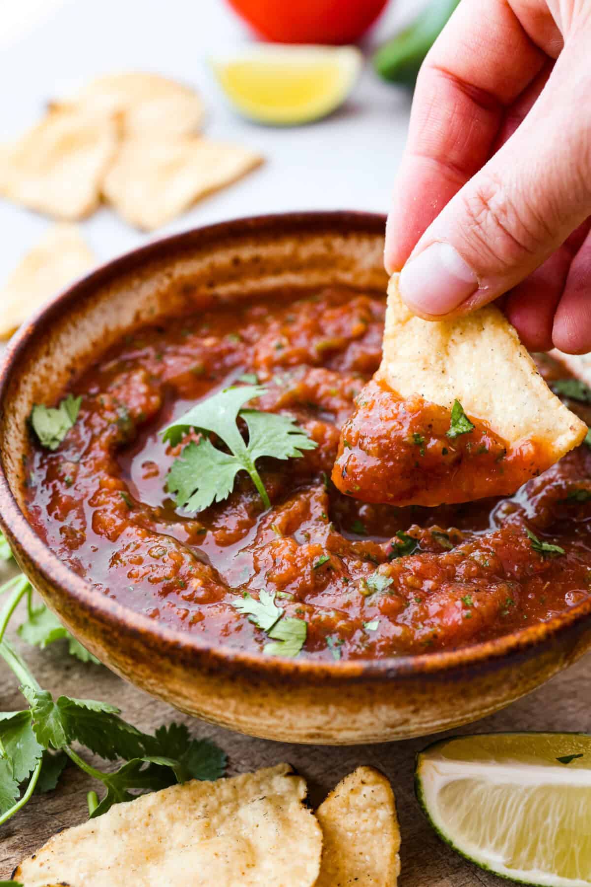 Best Blender Salsa is restaurant-quality salsa that is made right in your blender! It only takes 5 minutes and is truly the very best out there! This vibrant and refreshing salsa has the perfect blend of sweet, spicy elements. Close up shot of someone dipping a chip into bowl of salsa.