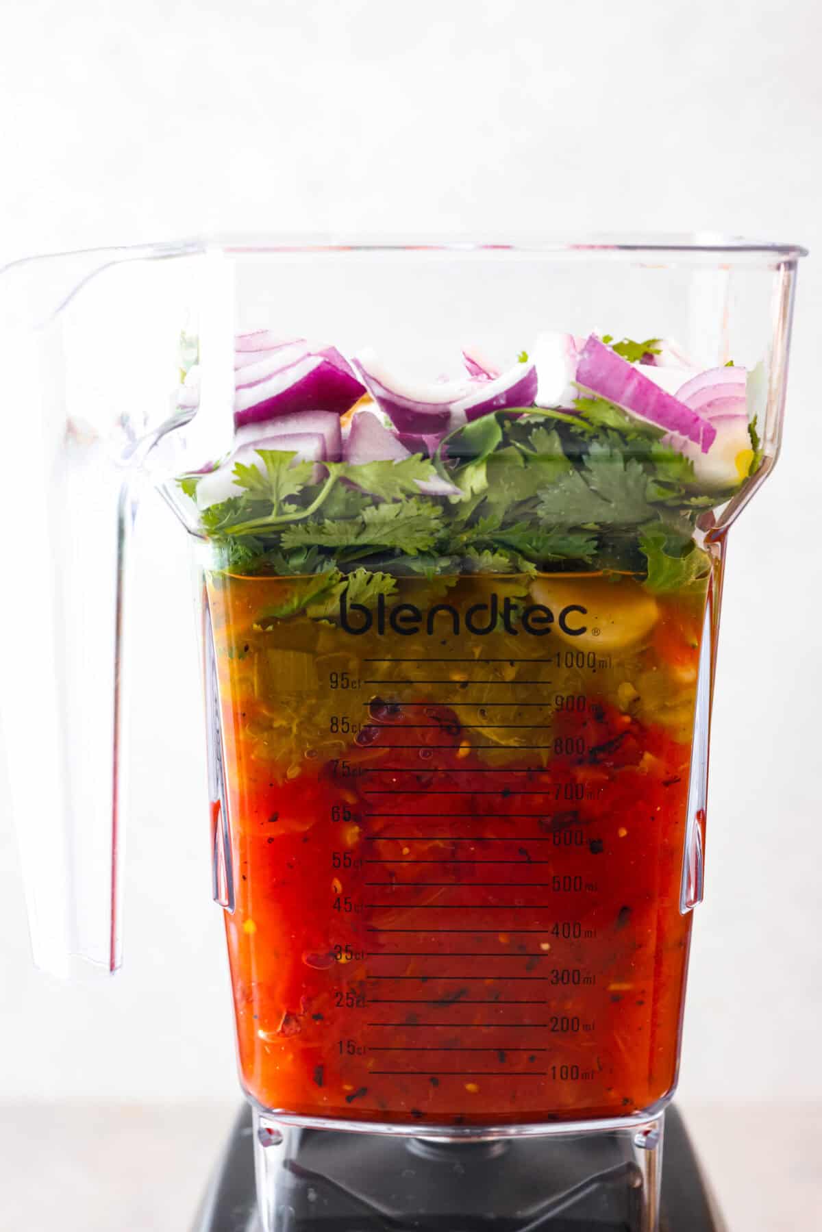 Best Blender Salsa is restaurant-quality salsa that is made right in your blender! It only takes 5 minutes and is truly the very best out there! This vibrant and refreshing salsa has the perfect blend of sweet, spicy elements. Side view of blender filled with fresh ingredients.