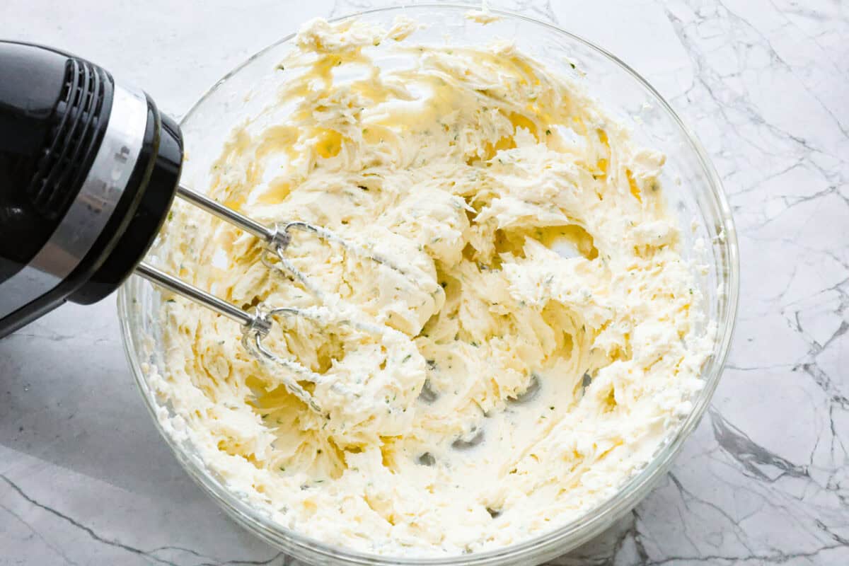 Boursin cheese is soft, creamy, and bursting with herbal flavor. Its texture is similar to cream cheese, making it incredibly versatile. It shines as a dip, enhances pasta dishes, complements meats, enriches sauces and soups, and so much more! Overhead shot of a hand mixer mixing Boursin cheese ingredients together.