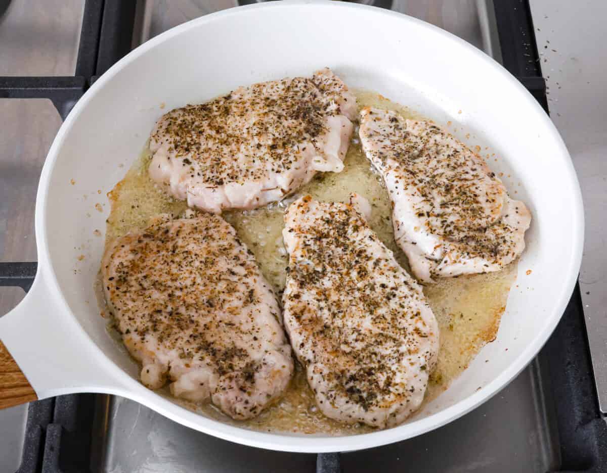 Boursin Pork Chops are savory, tender, and covered in a delicious cheesy cream sauce. This one-pan recipe is the perfect easy main that can be on your dinner table in just 30 minutes! Angle shot of seasoned pork chops in pan.