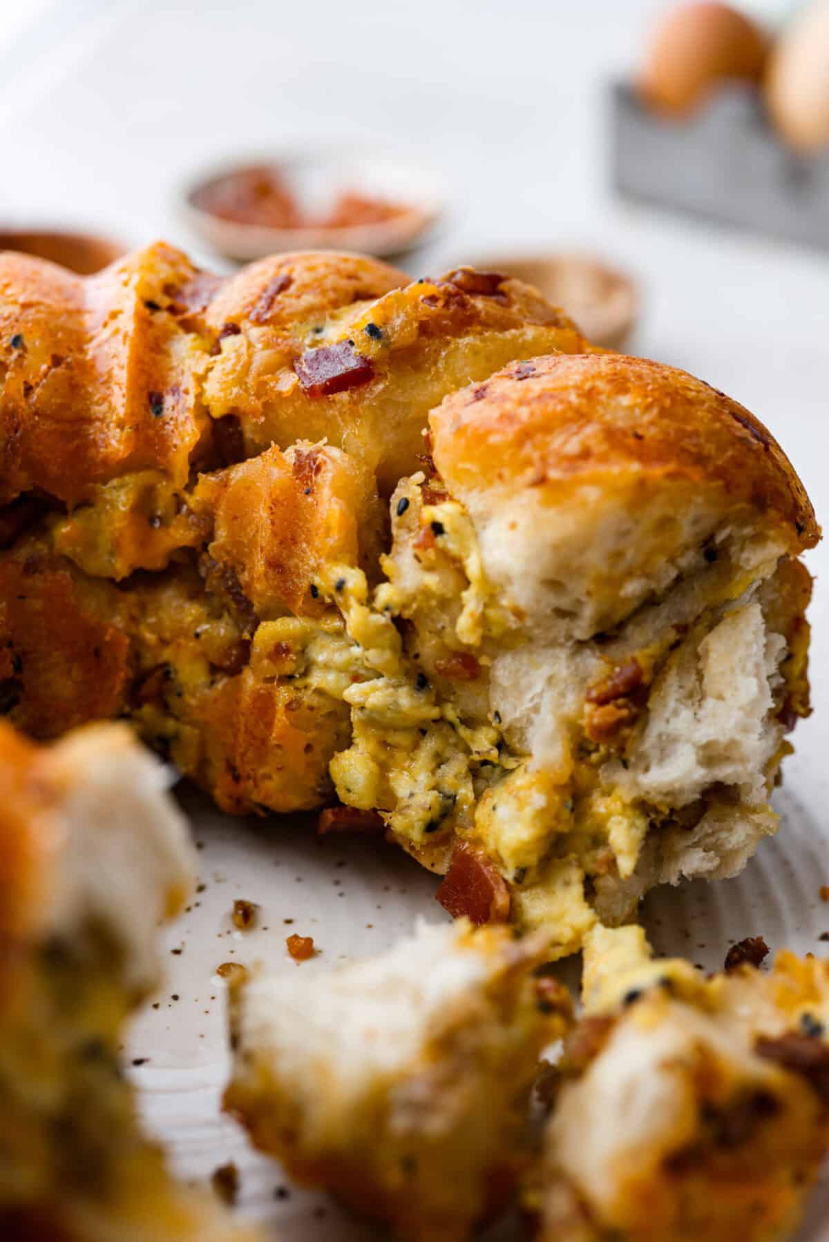 Rise and shine to Breakfast Monkey Bread with delicious savory flavors! It’s made with Grands biscuits, eggs, sausage, bacon, and cheese, all baked in a bundt pan. The result is crowd-pleasing pull-apart bread that everyone will devour! Close up shot of the breakfast monkey bread with piece taken out.