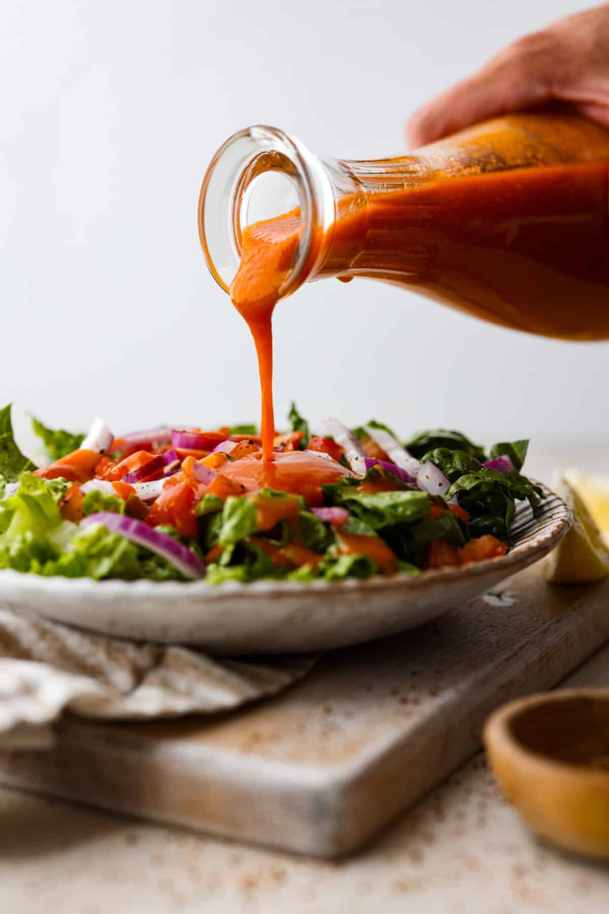 Delicious Catalina French Dressing will give your salad the perfect tangy, sweet flavor! It comes together quickly with a few simple ingredients you probably already have in your kitchen! Once you try it, you will want to have it on repeat! Side shot of someone pouring dressing over a plated salad.