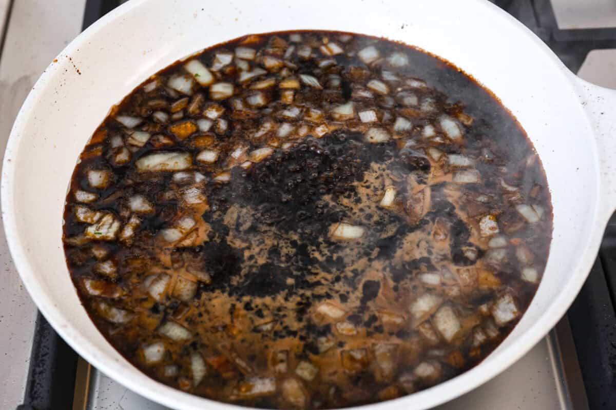 Chicken Adobo is a tangy, salty, sweet, and spicy Filipino dish. This meal is easy to make and requires just a few simple ingredients. It's sure to become a family favorite! Angle shot of sauce and onions boiling in the skillet.