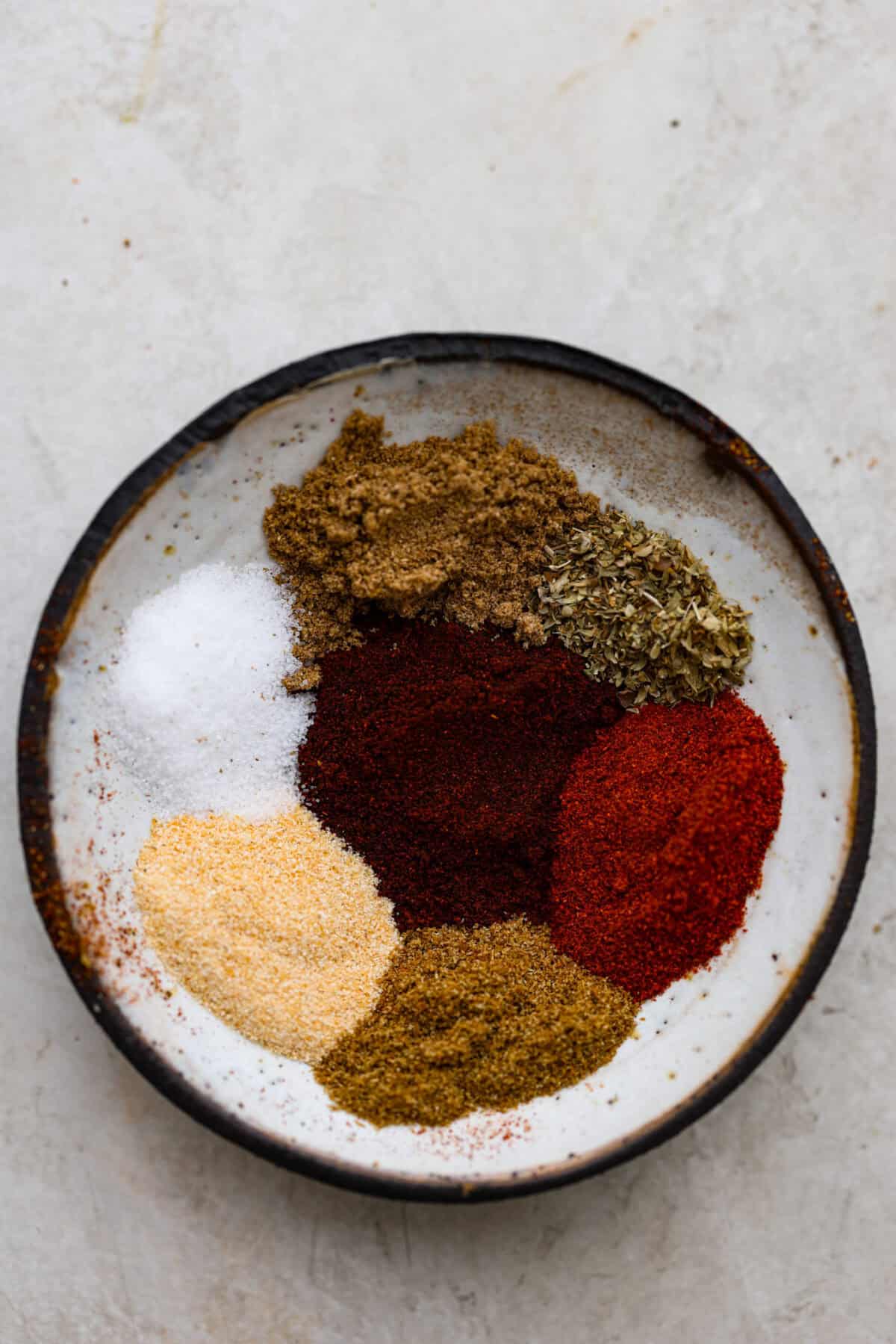 Enjoy a perfect blend of smoky and spicy flavors with this homemade Chipotle Seasoning! Featuring bold spices like chipotle powder, paprika, cumin, garlic powder, oregano, and more, this mix delivers a major flavor boost. Try it on everything from chicken to ground beef! Close up shot of separated ingredients in bowl.