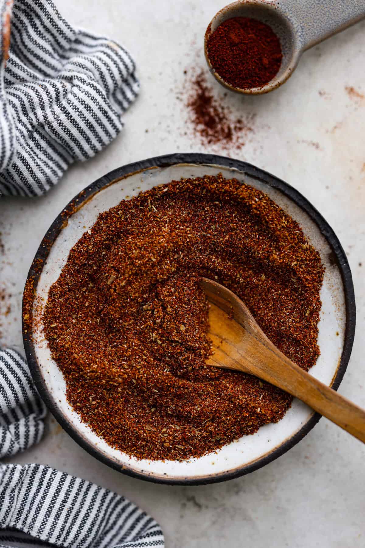 Enjoy a perfect blend of smoky and spicy flavors with this homemade Chipotle Seasoning! Featuring bold spices like chipotle powder, paprika, cumin, garlic powder, oregano, and more, this mix delivers a major flavor boost. Try it on everything from chicken to ground beef! Overhead shot of mixed chipotle seasoning in a bowl with wooden spoon sticking out of it.