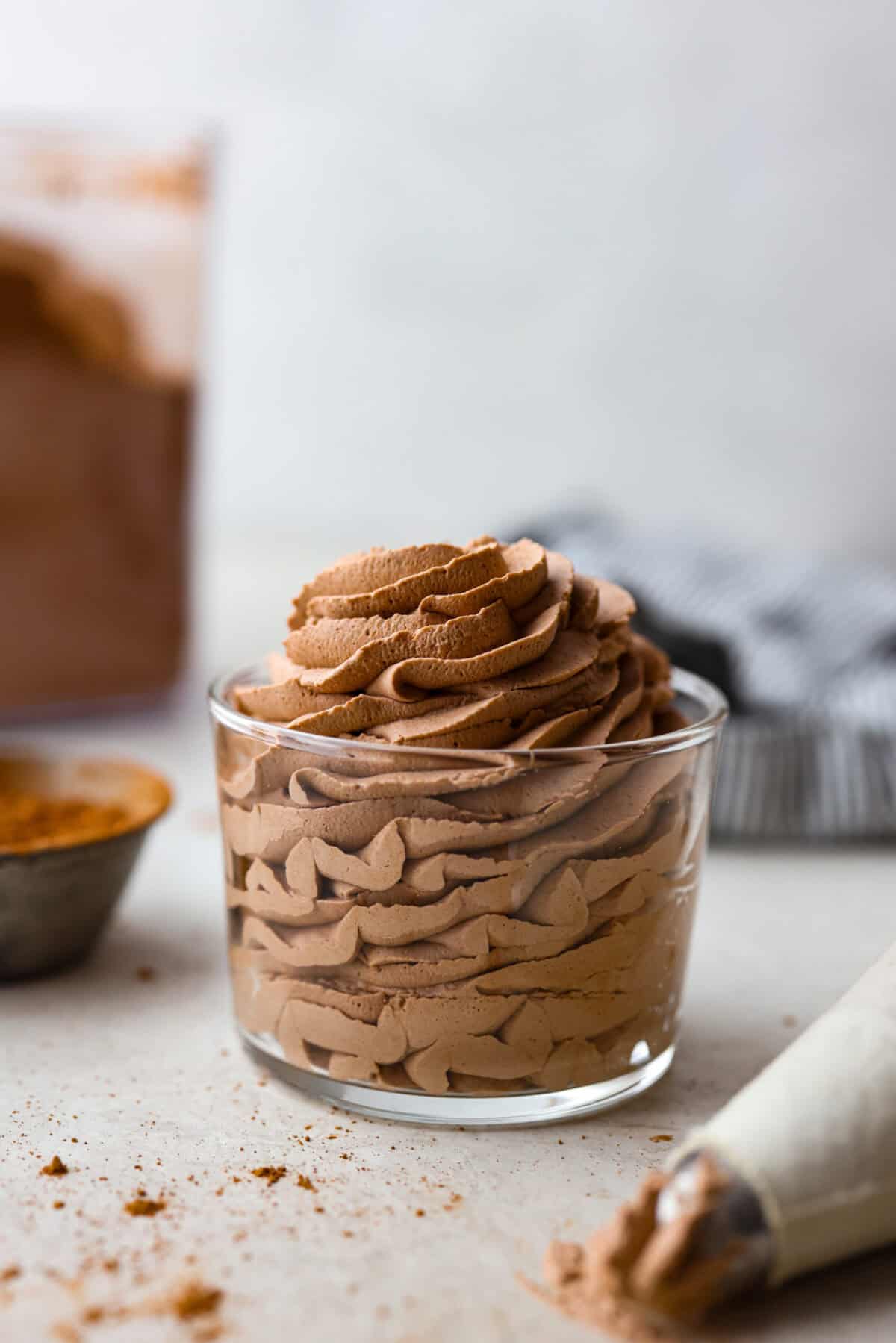 Fluffy Chocolate Whipped Cream is a wonderful combination of chocolate with fresh whipped cream! Itโs the perfect topping for fruit, waffles, pie, cupcakes and so much more! Side view of a glass with piped chocolate whipped cream inside.