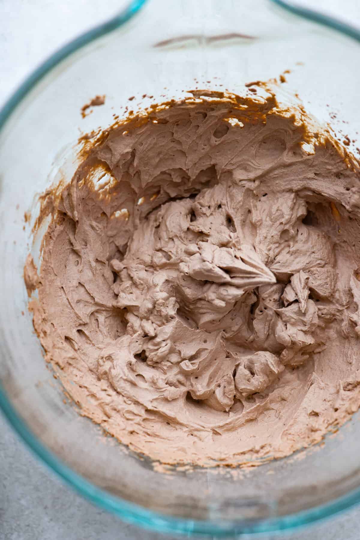 Fluffy Chocolate Whipped Cream is a wonderful combination of chocolate with fresh whipped cream! Itโs the perfect topping for fruit, waffles, pie, cupcakes and so much more! Overhead shot of chocolate whipped cream in glass bowl.
