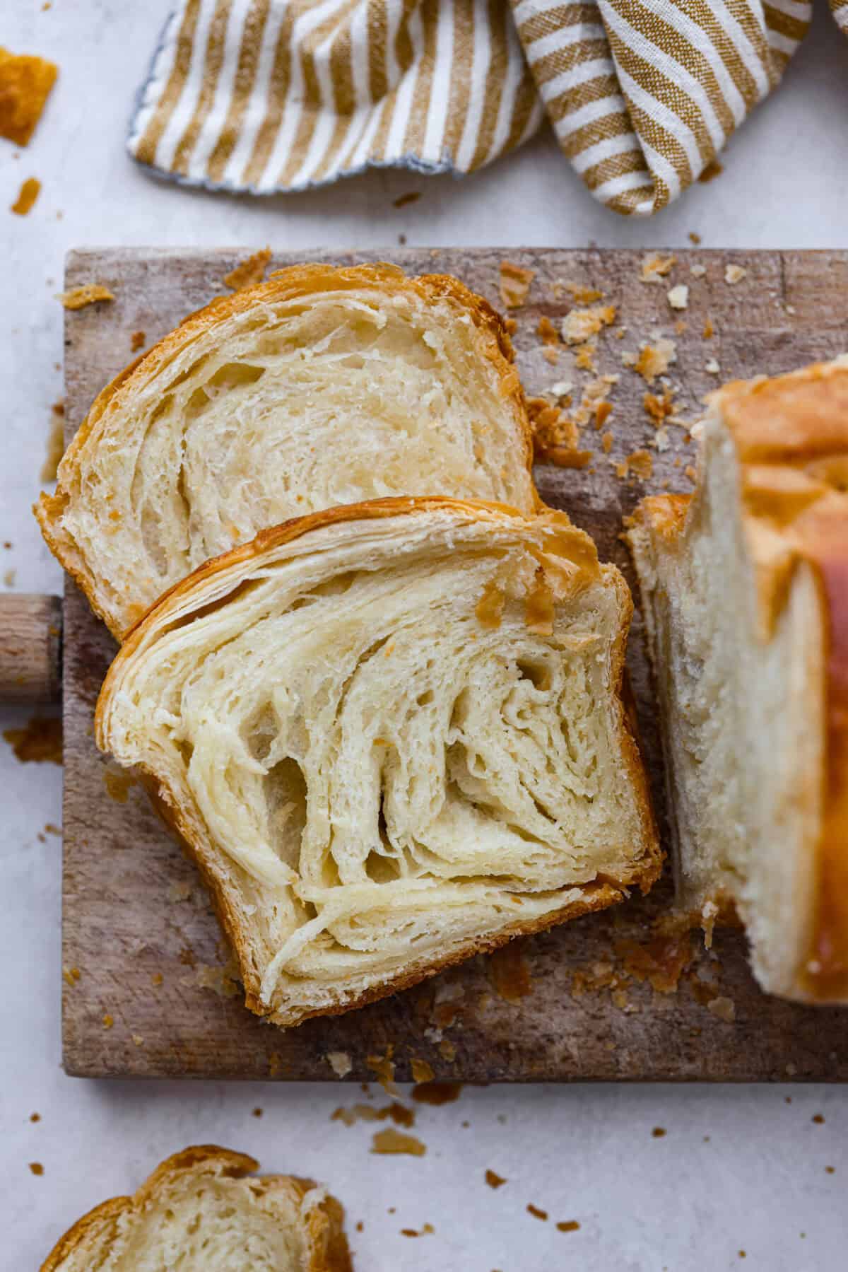 Croissant Bread is beautiful and fluffy with crispy, flaky layers on the outside. It's also one of the most delicious breads you'll ever taste - it will be love at first bite! Add it to your next brunch spread and use it to make French toast, sandwiches, and breakfast casseroles! Overhead shot of slices of croissant bread on cutting board.