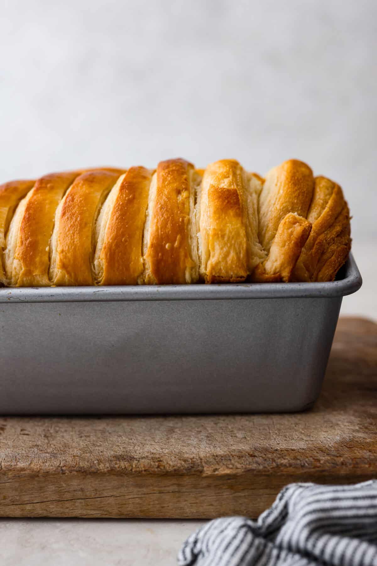 Croissant Bread is beautiful and fluffy with crispy, flaky layers on the outside. It's also one of the most delicious breads you'll ever taste - it will be love at first bite! Add it to your next brunch spread and use it to make French toast, sandwiches, and breakfast casseroles! Side shot of baked croissant bread with browned top.