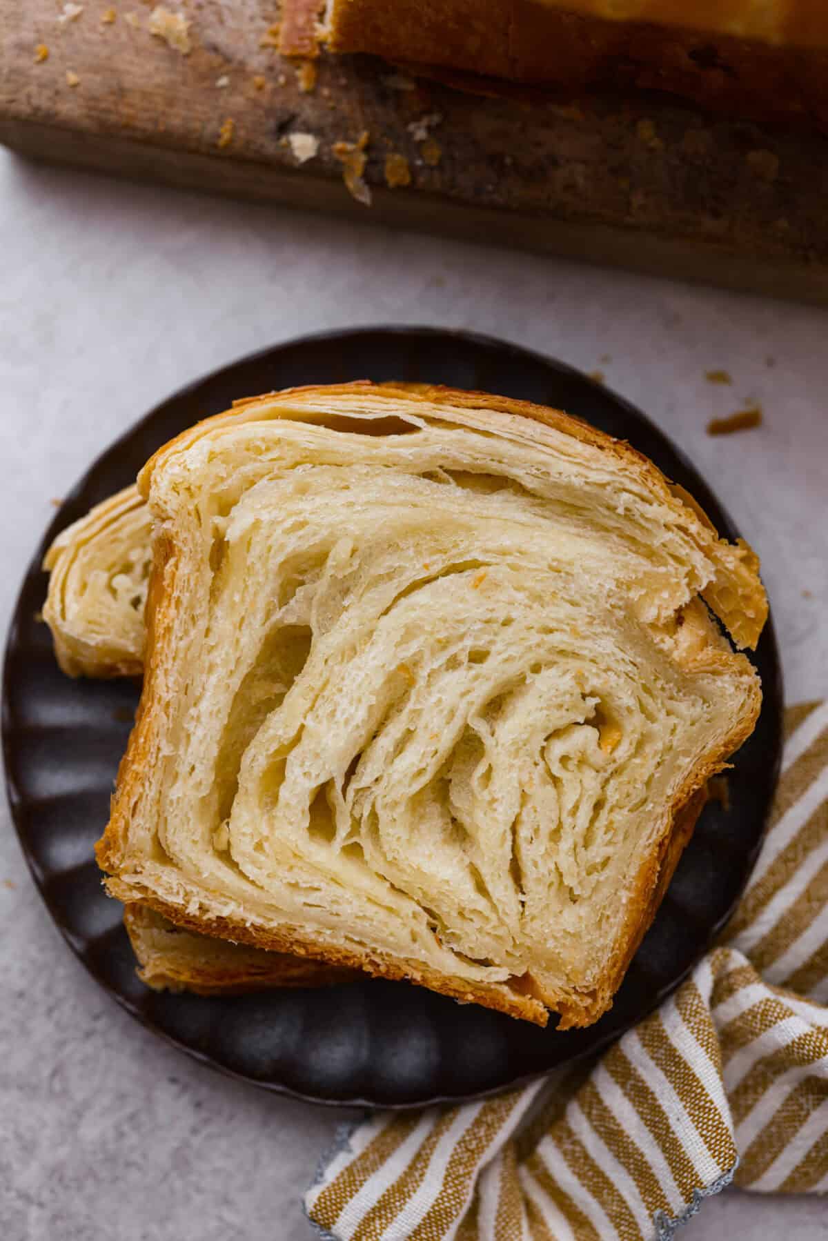 Croissant Bread is beautiful and fluffy with crispy, flaky layers on the outside. It's also one of the most delicious breads you'll ever taste - it will be love at first bite! Add it to your next brunch spread and use it to make French toast, sandwiches, and breakfast casseroles! Overhead shot of plated slices of croissant bread.