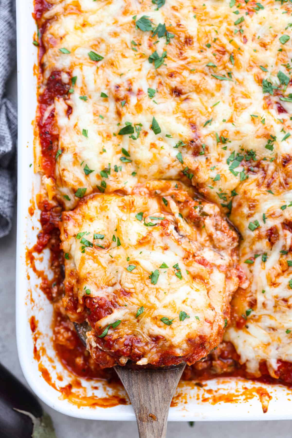 Eggplant Lasagna is a delicious low-carb way to enjoy the classic flavors of lasagna! The tender eggplant layers are loaded with meat sauce, a creamy ricotta mixture, and lots of melty cheese. You won't even miss the noodles! Close top view of the eggplant lasagna in a casserole dish with a wood serving spatula.