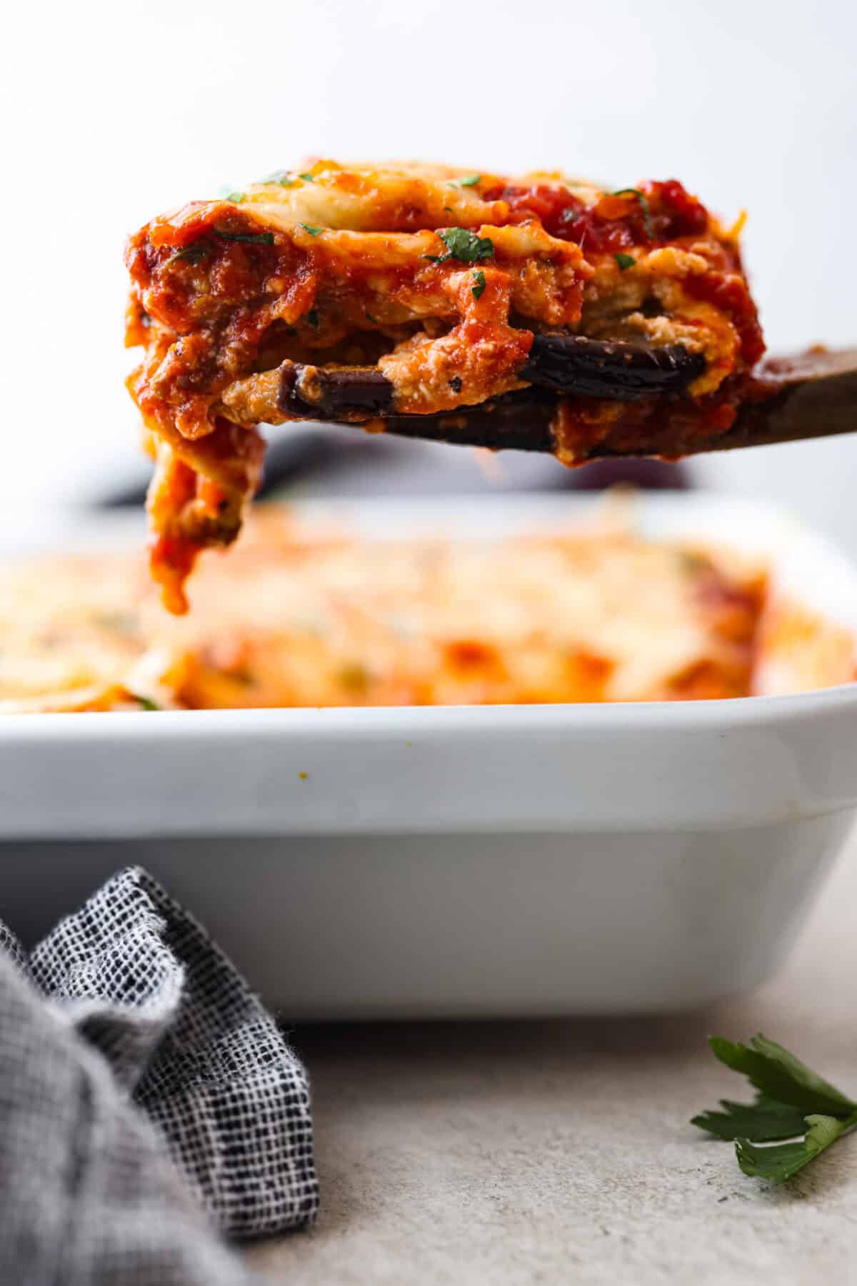 Eggplant Lasagna is a delicious low-carb way to enjoy the classic flavors of lasagna! The tender eggplant layers are loaded with meat sauce, a creamy ricotta mixture, and lots of melty cheese. You won't even miss the noodles! Close side view of a slice of eggplant lasagna lifting from the dish.