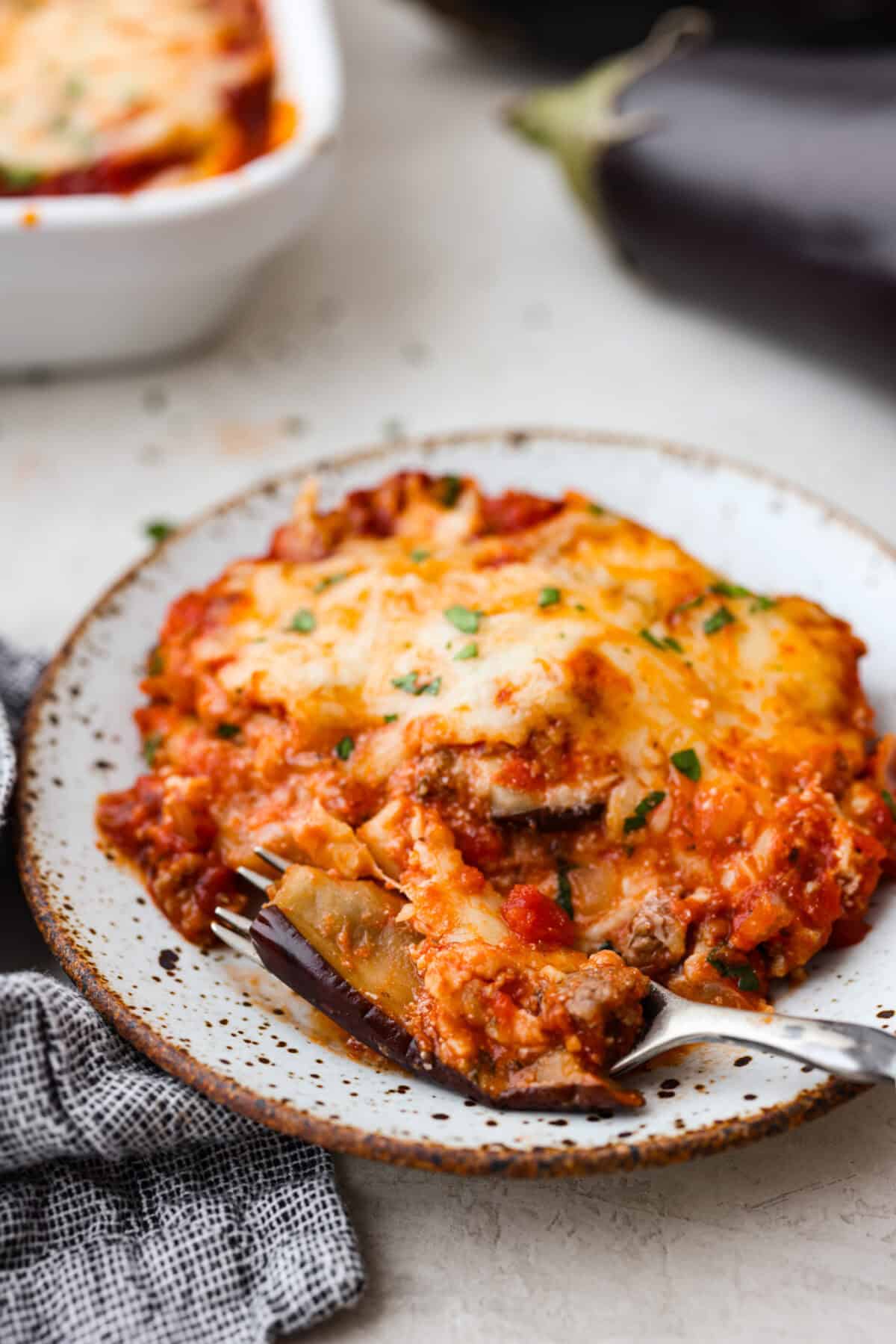 Eggplant Lasagna is a delicious low-carb way to enjoy the classic flavors of lasagna! The tender eggplant layers are loaded with meat sauce, a creamy ricotta mixture, and lots of melty cheese. You won't even miss the noodles! Close view of a slice of eggplant lasagna on a plate with a fork.
