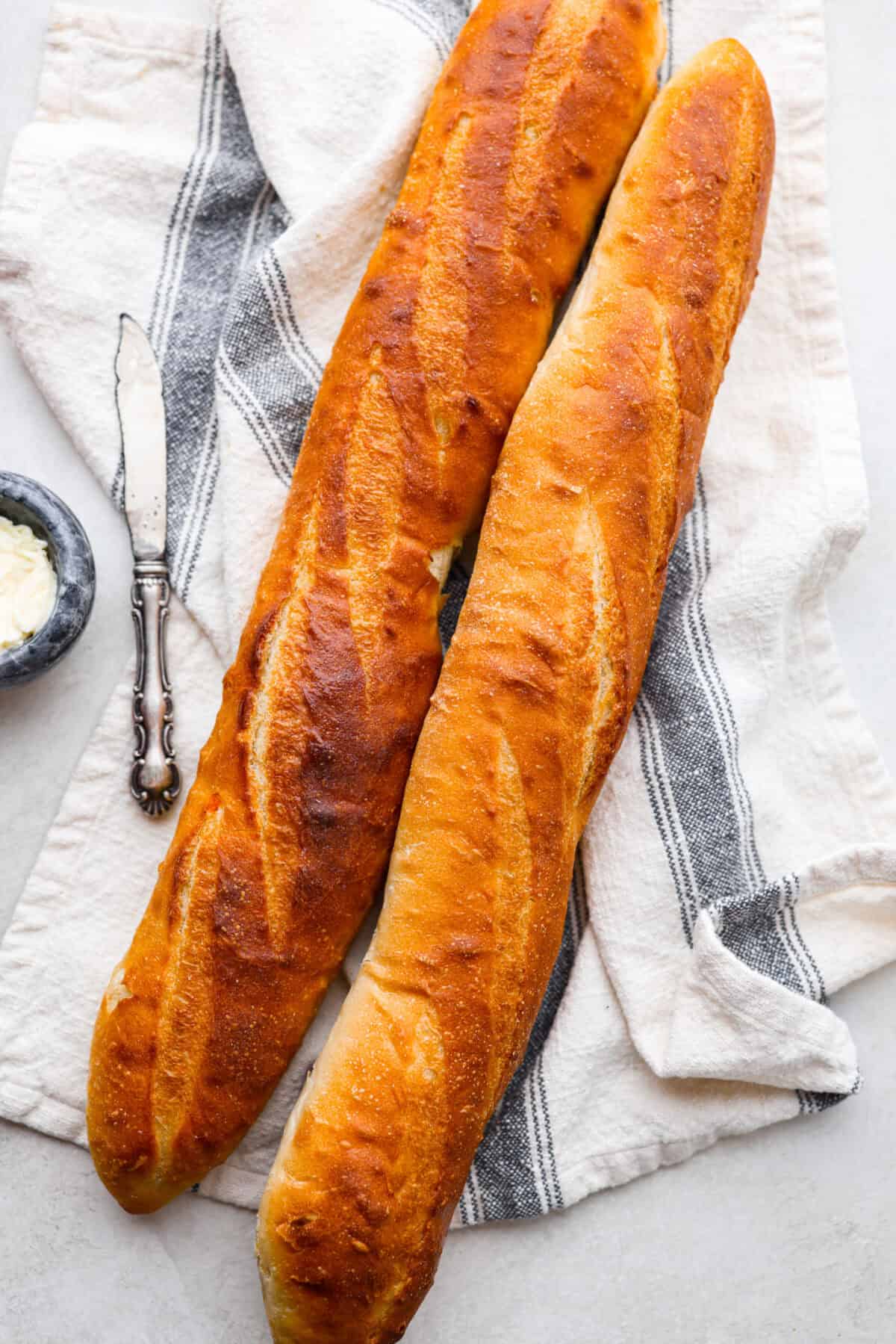This French baguette recipe is super easy and will change your life! It has a perfect crusty outside and tender, soft inside, perfect for your bread cravings. Overhead shot of two french Baguettes.
