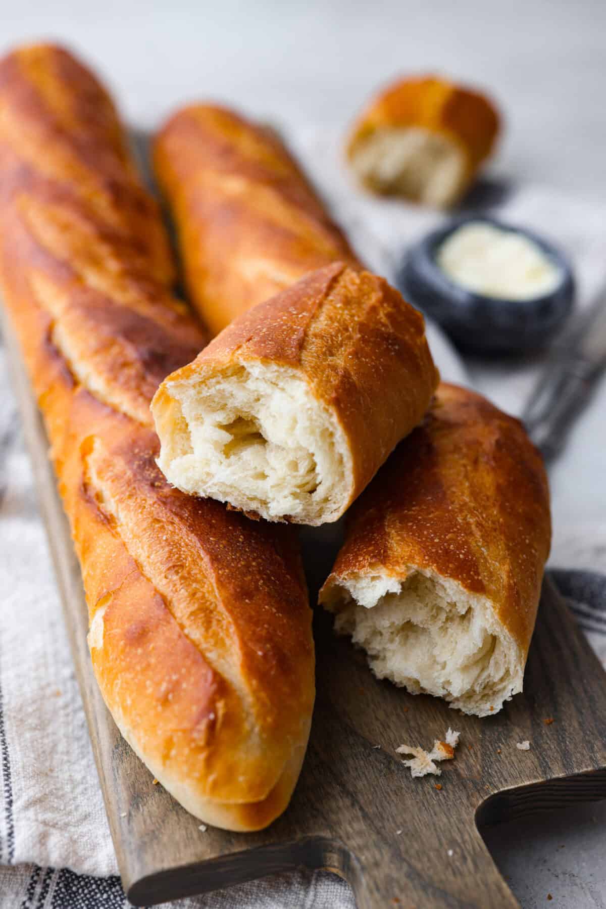 This French baguette recipe is super easy and will change your life! It has a perfect crusty outside and tender, soft inside, perfect for your bread cravings. Angle shot of baguettes on a cutting board, one is pulled apart.