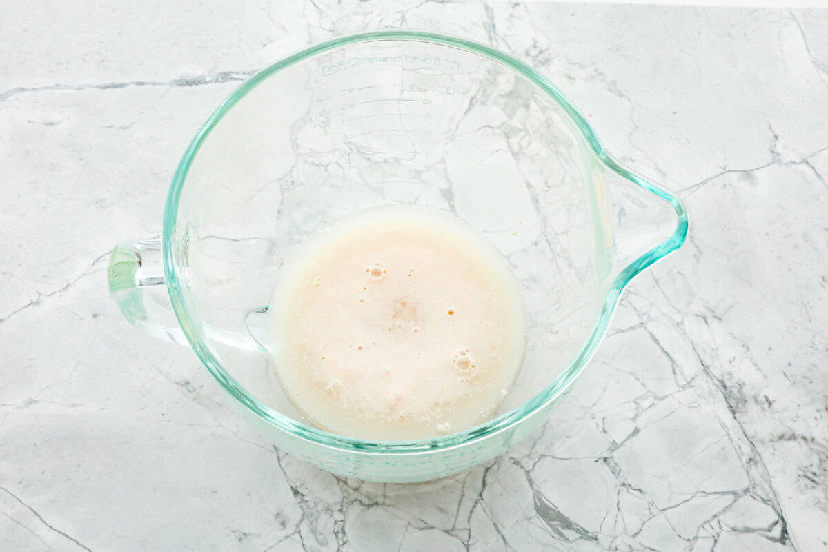 This French baguette recipe is super easy and will change your life! It has a perfect crusty outside and tender, soft inside, perfect for your bread cravings. Overhead shot of yeast, water and honey in a bowl.
